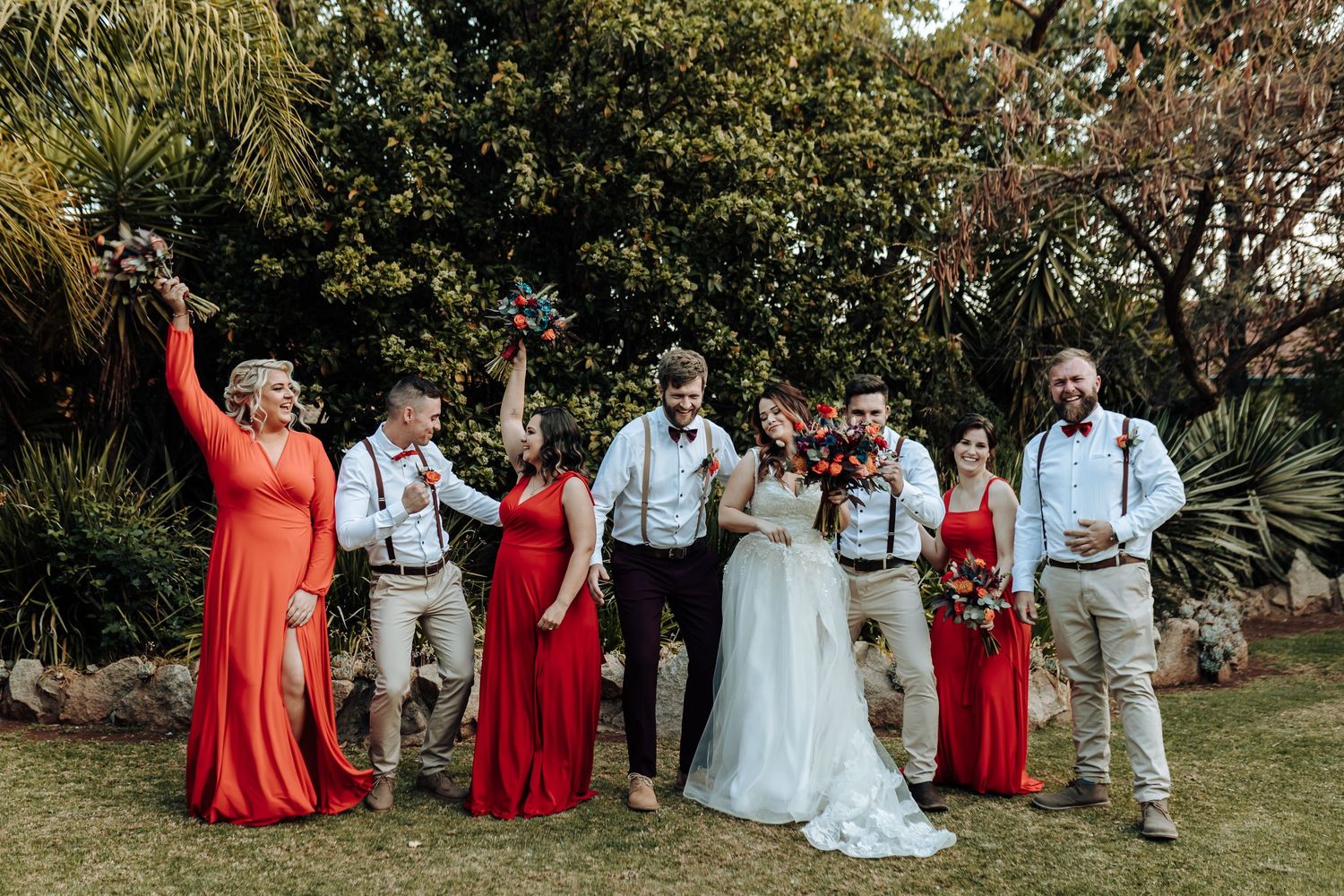 Fun wedding party photo with bridal party in red dresses and groomsmen in light colored attire.