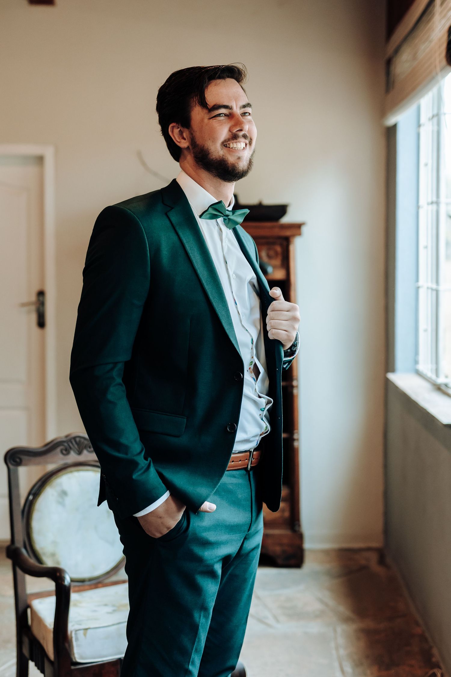Emerald green tuxedo with bow tie styled against bright window in classic room setting.