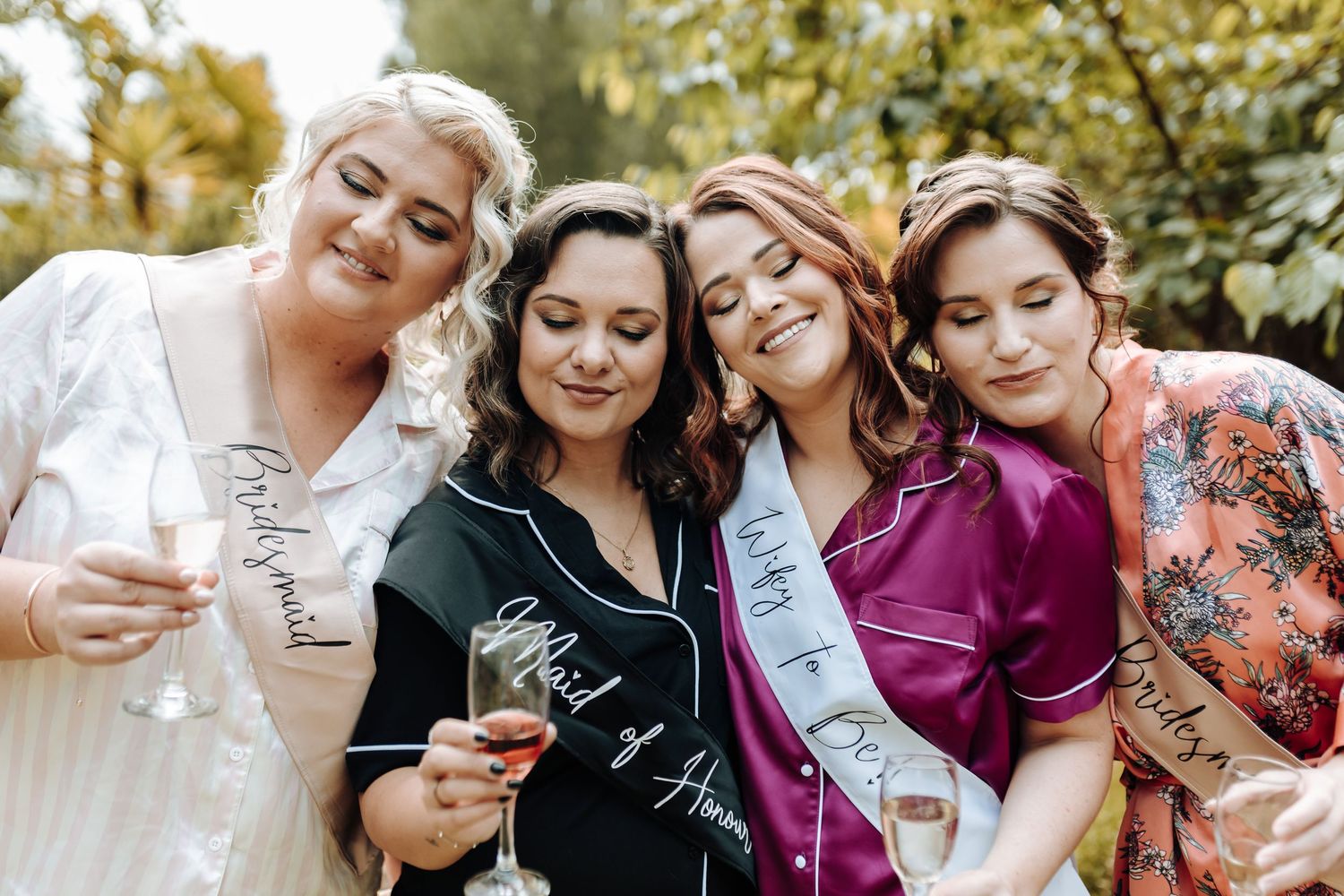 Friends share an intimate moment while toasting with drinks in a garden setting.