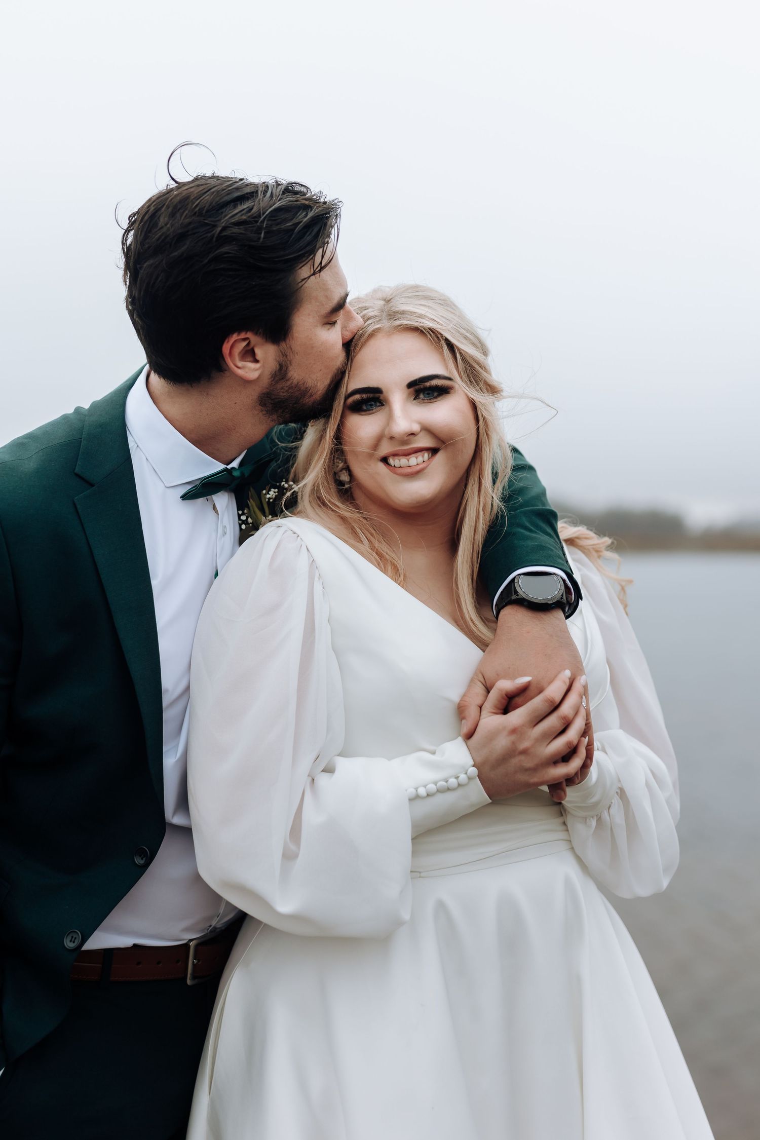 A joyful wedding moment captured as couple embraces in formal attire by the waterfront.
