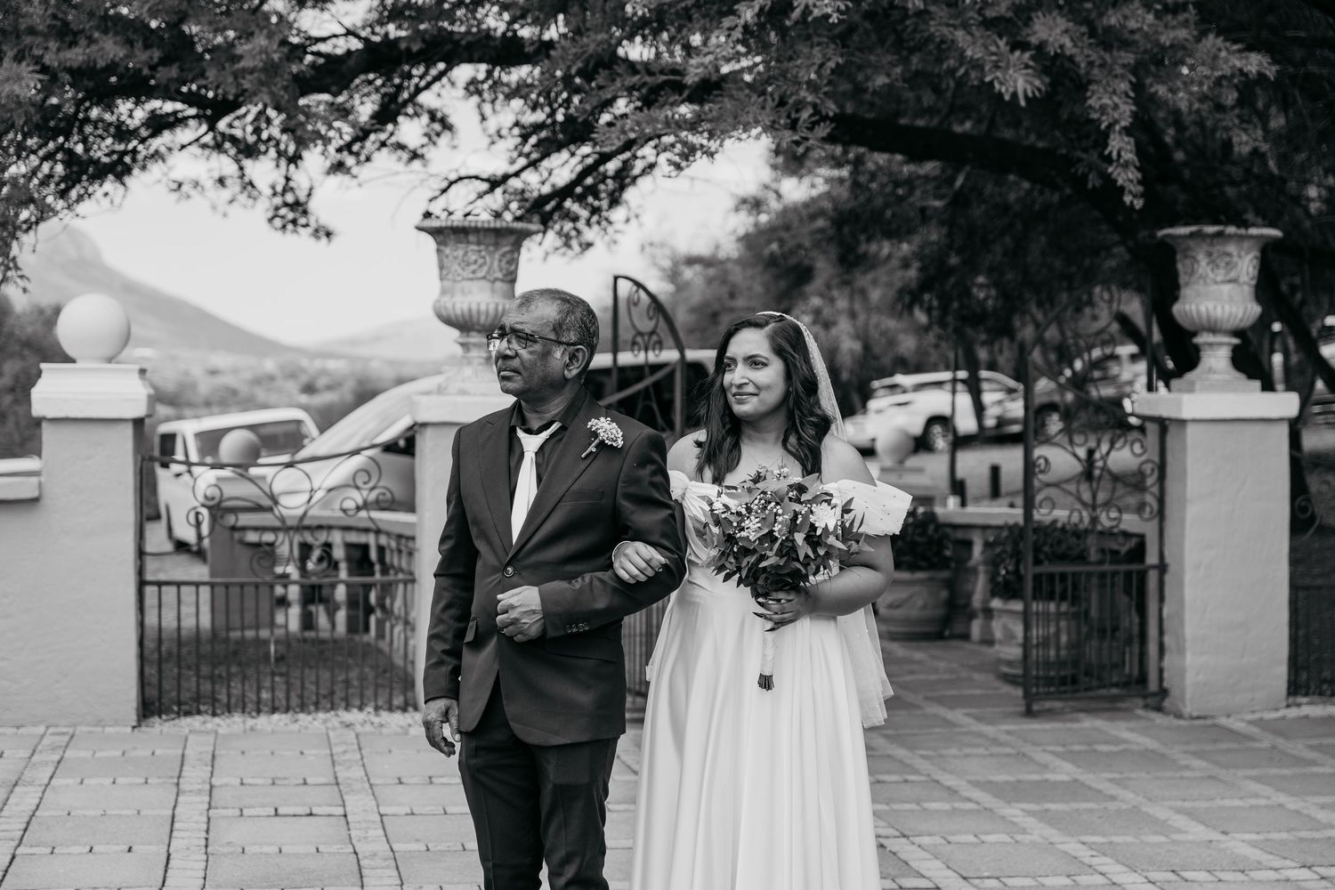 Black and white photo of two people walking through ornate garden gates during wedding ceremony.