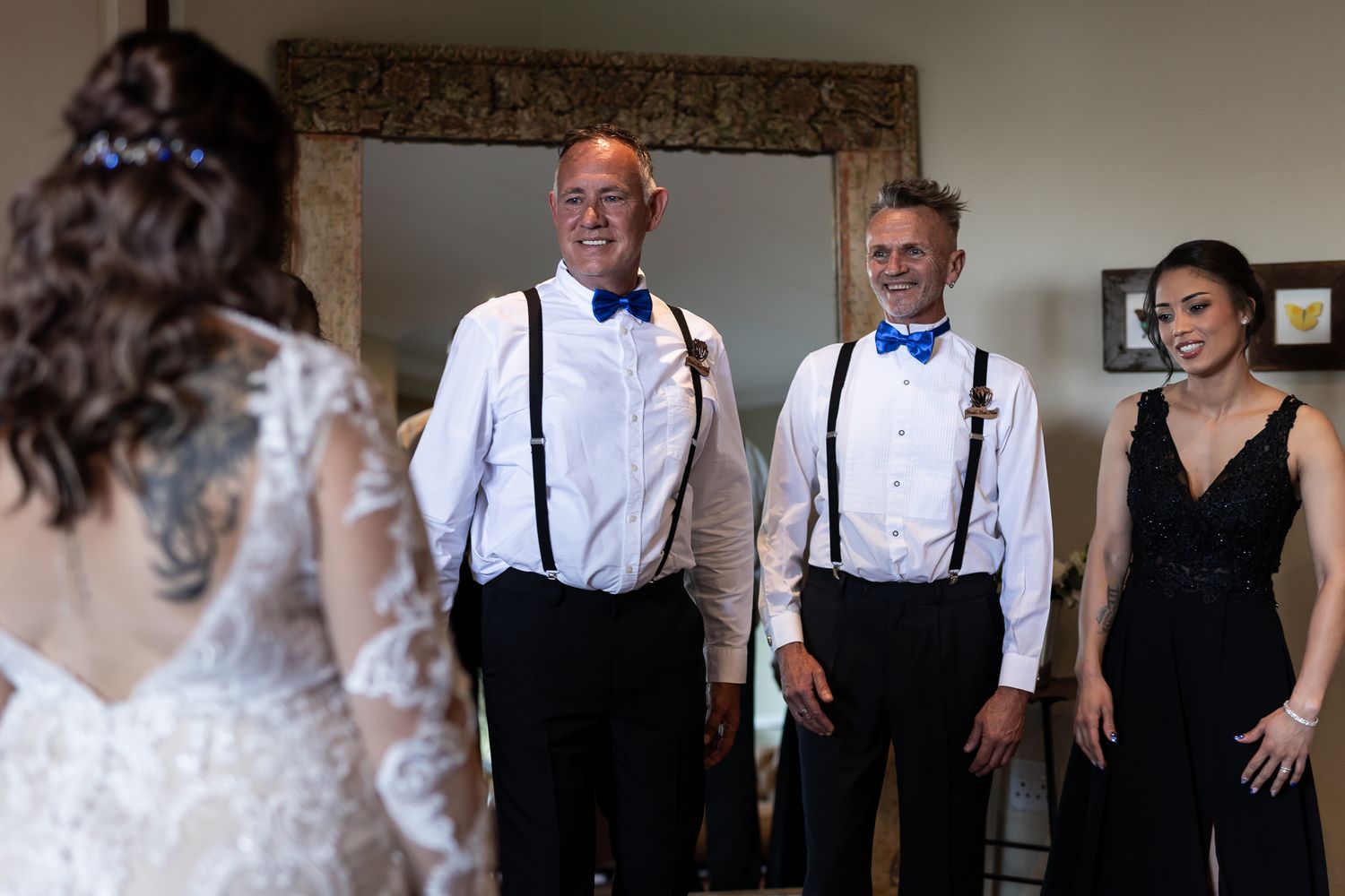 Wedding party members in formal attire gather around ornate mirror during pre-ceremony preparations.