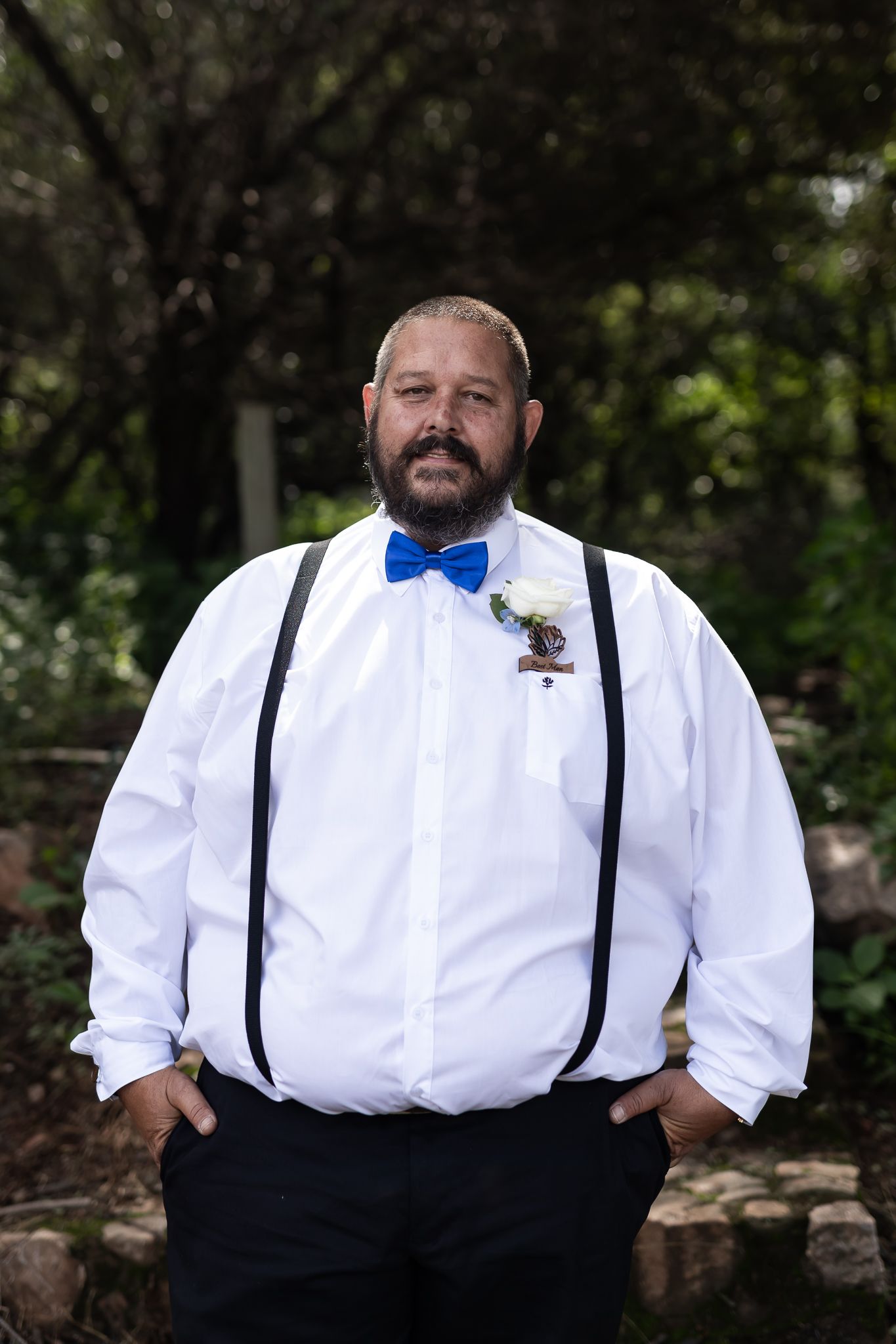 Groomsman in white shirt with blue bowtie and suspenders poses for wedding portrait.