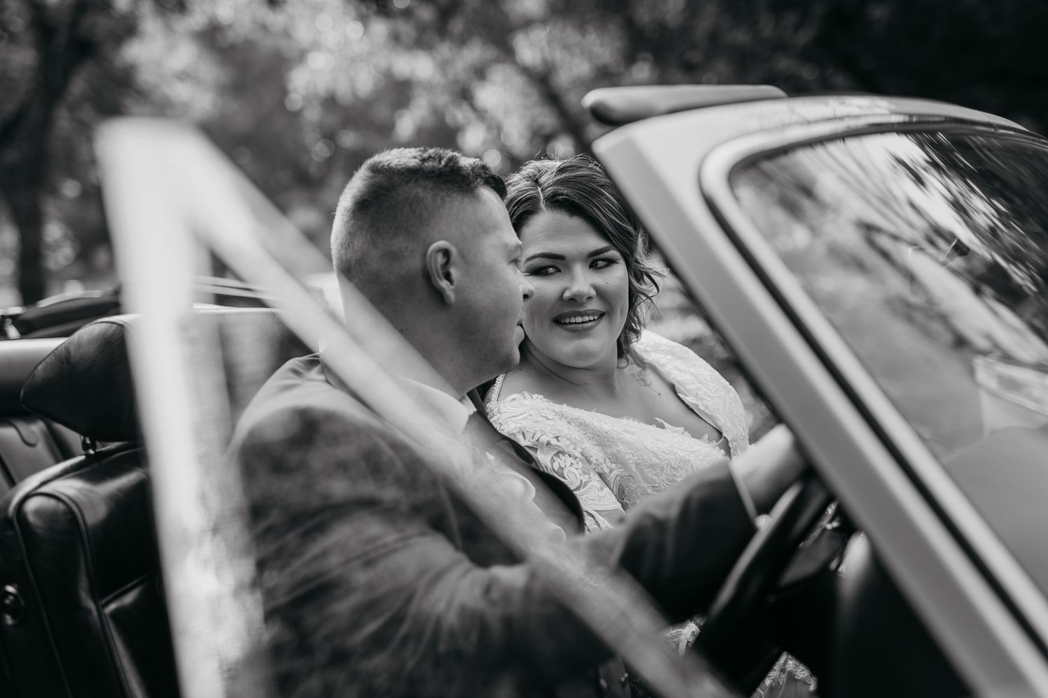 Black and white candid of newlyweds sharing intimate moment in classic car.