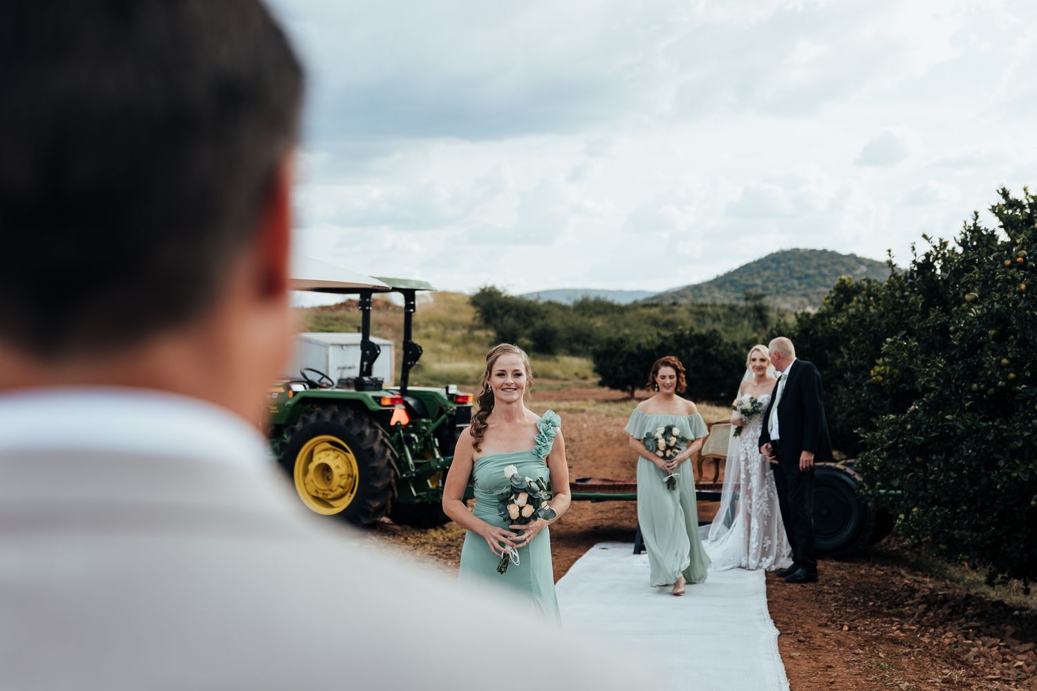 Wedding party approaches on tractor with mountain landscape in background.