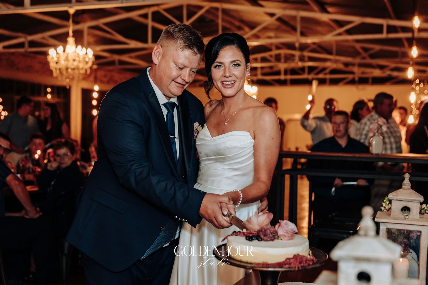 Bride and groom smiling while cutting their wedding cake at a romantic candlelit reception venue.