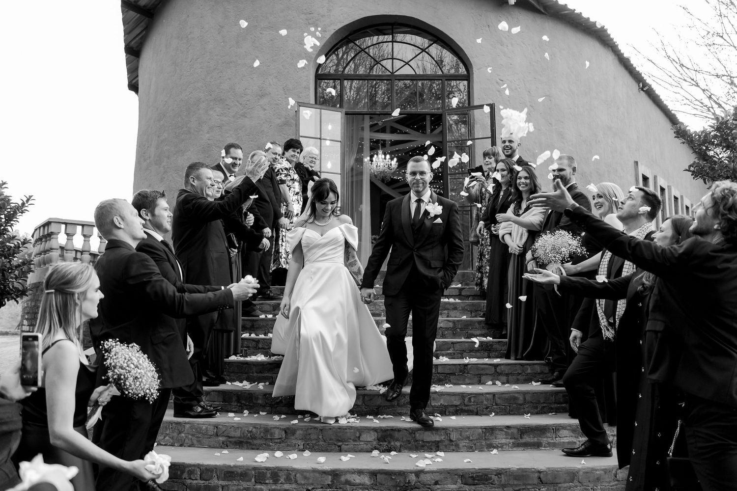 A newly married couple exits a church while guests throw confetti and celebrate on the stone steps.