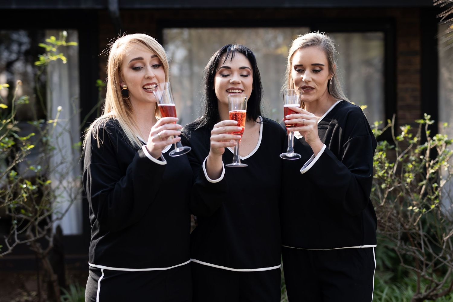 Three people in matching black sweaters share drinks and laughter together outdoors.