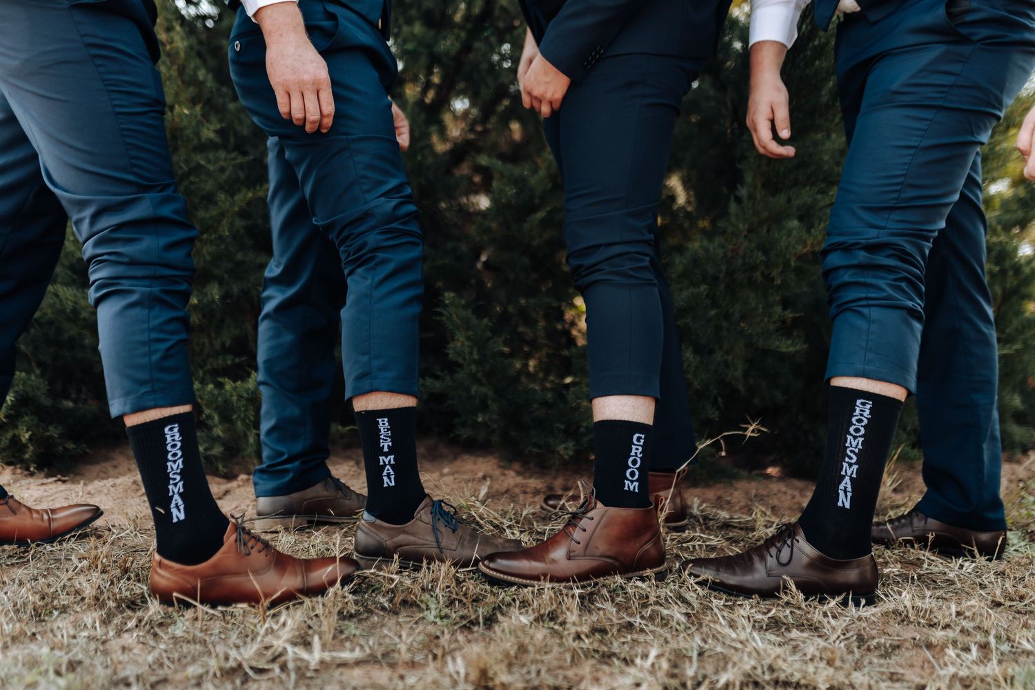 Row of people wearing dark blue jeans and assorted casual shoes standing outdoors.