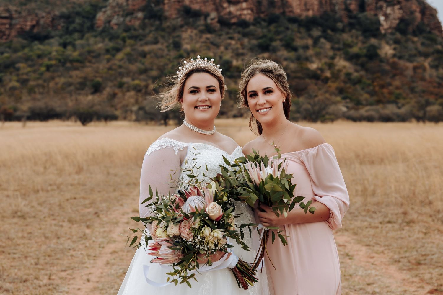 Bridal party in pink dresses holding bouquets and posing outdoors in a natural setting.