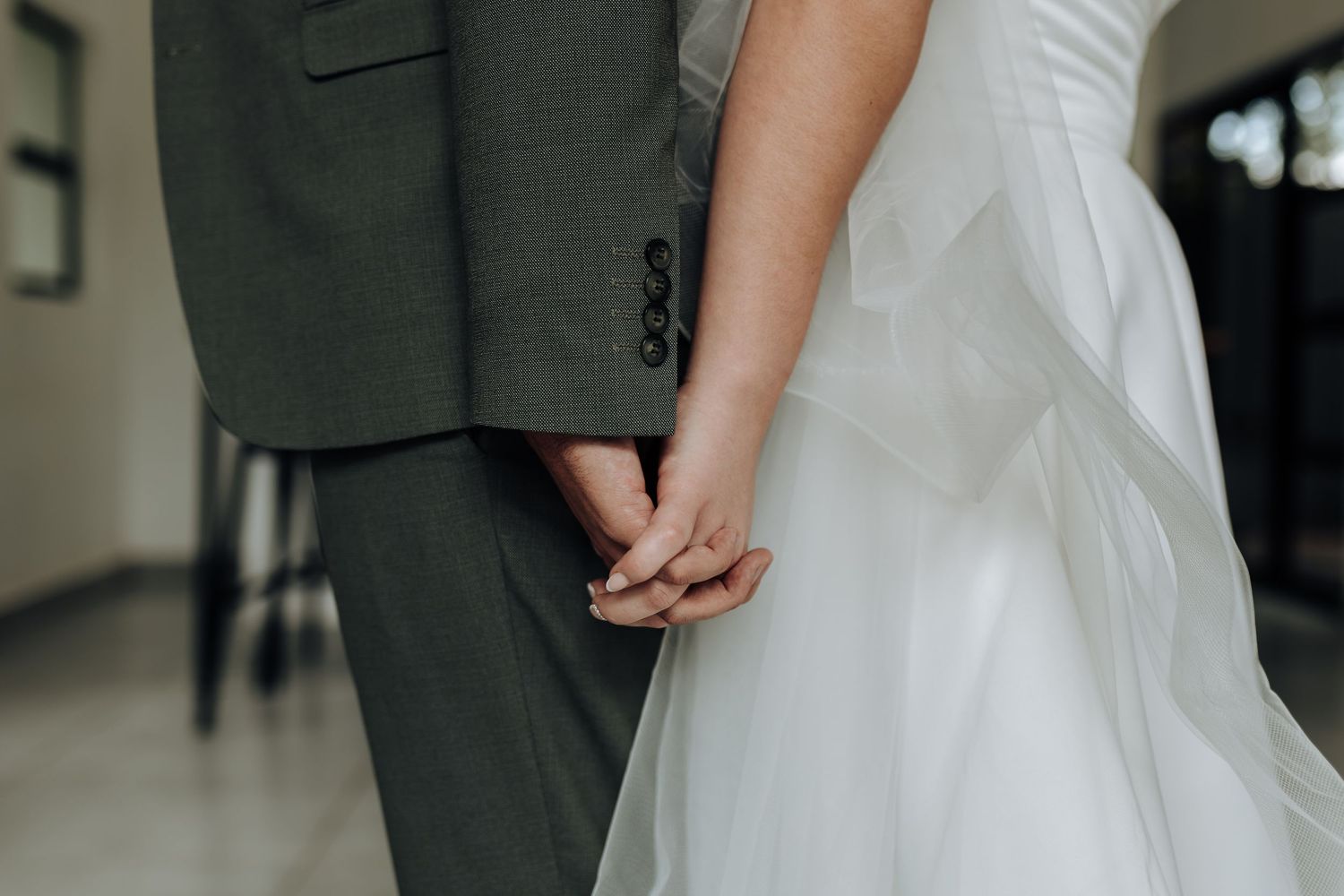 Wedding couple embracing in an elegant white interior with chandelier overhead.