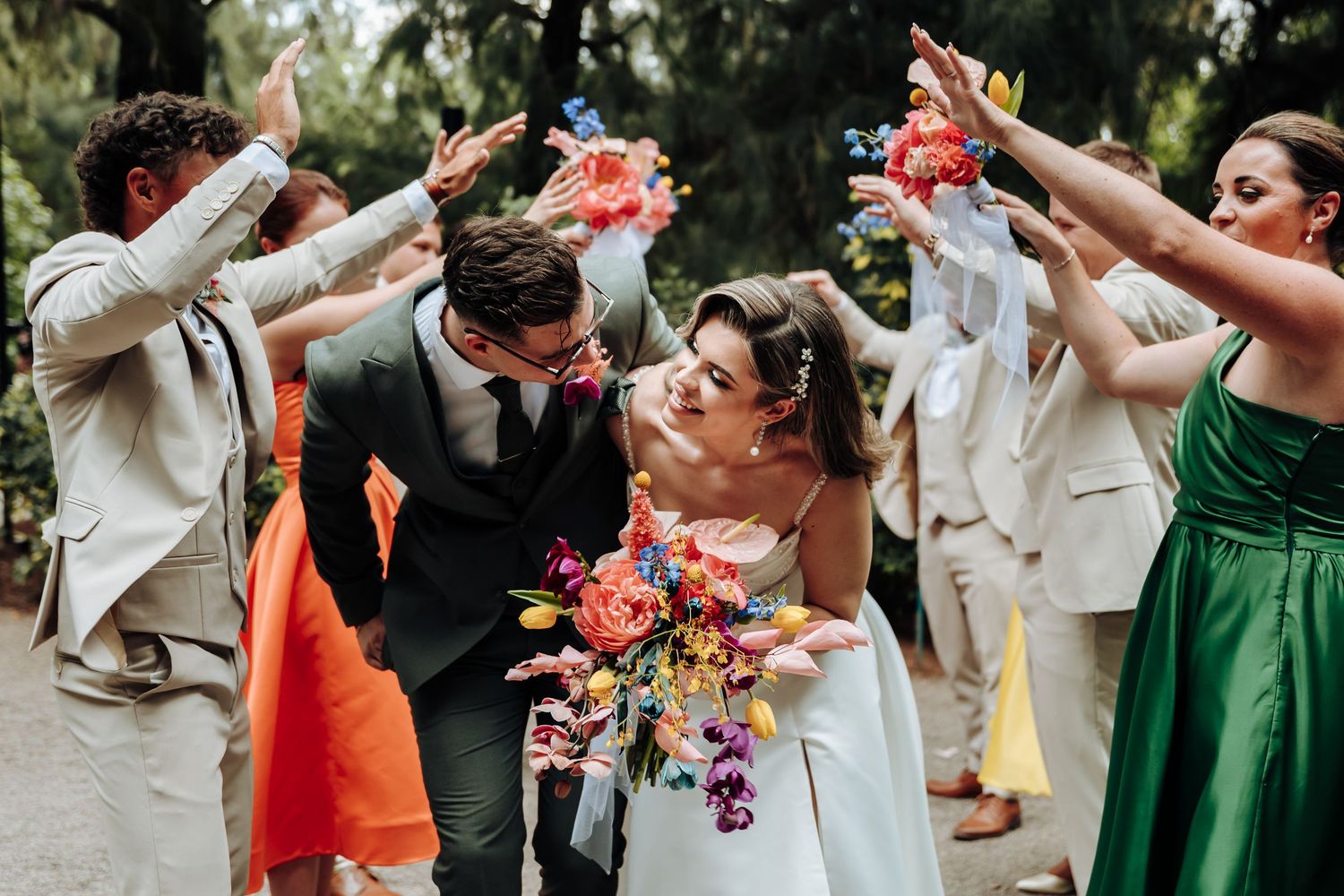 A festive wedding party celebration with people throwing pink confetti in an outdoor garden setting.