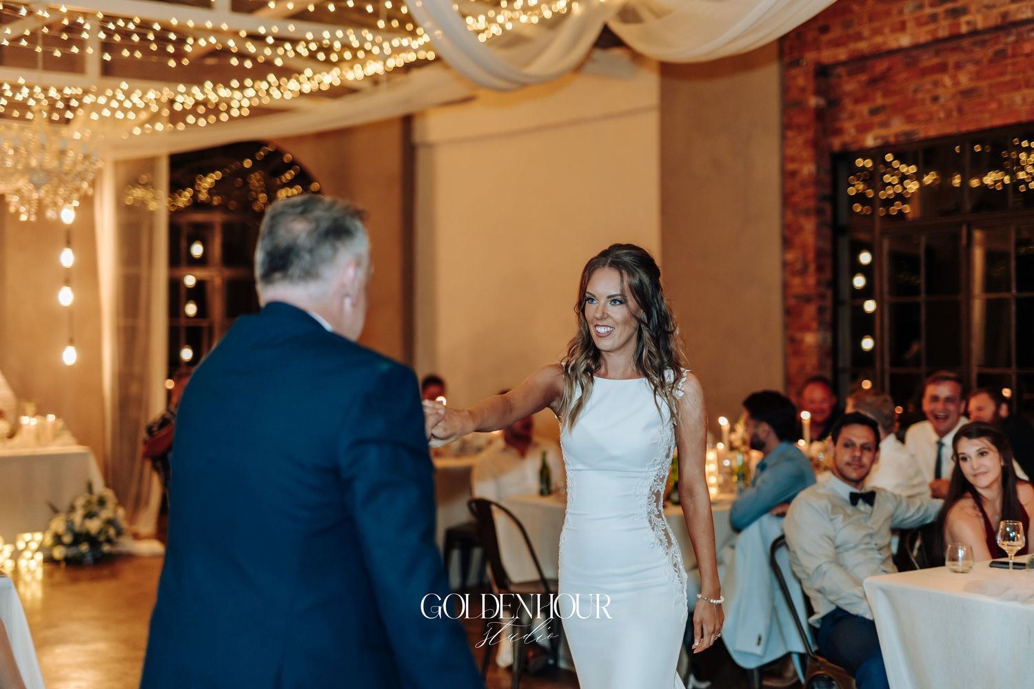Wedding guests dancing at an indoor reception with string lights and elegant decor.