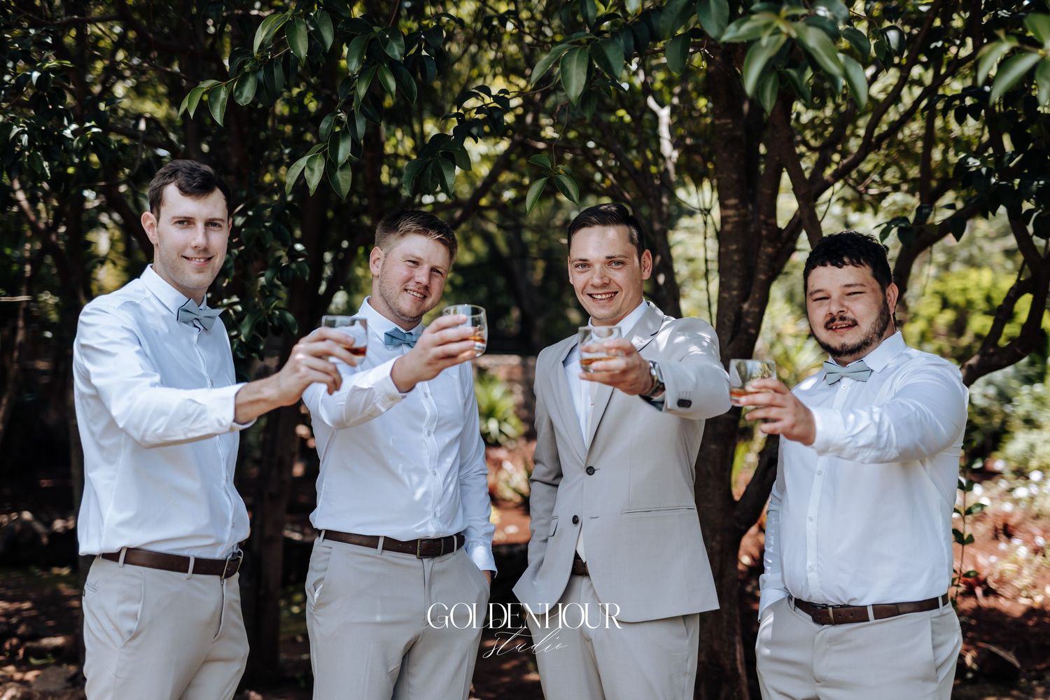 Groomsmen in light gray suits pose together outdoors during a wedding celebration.