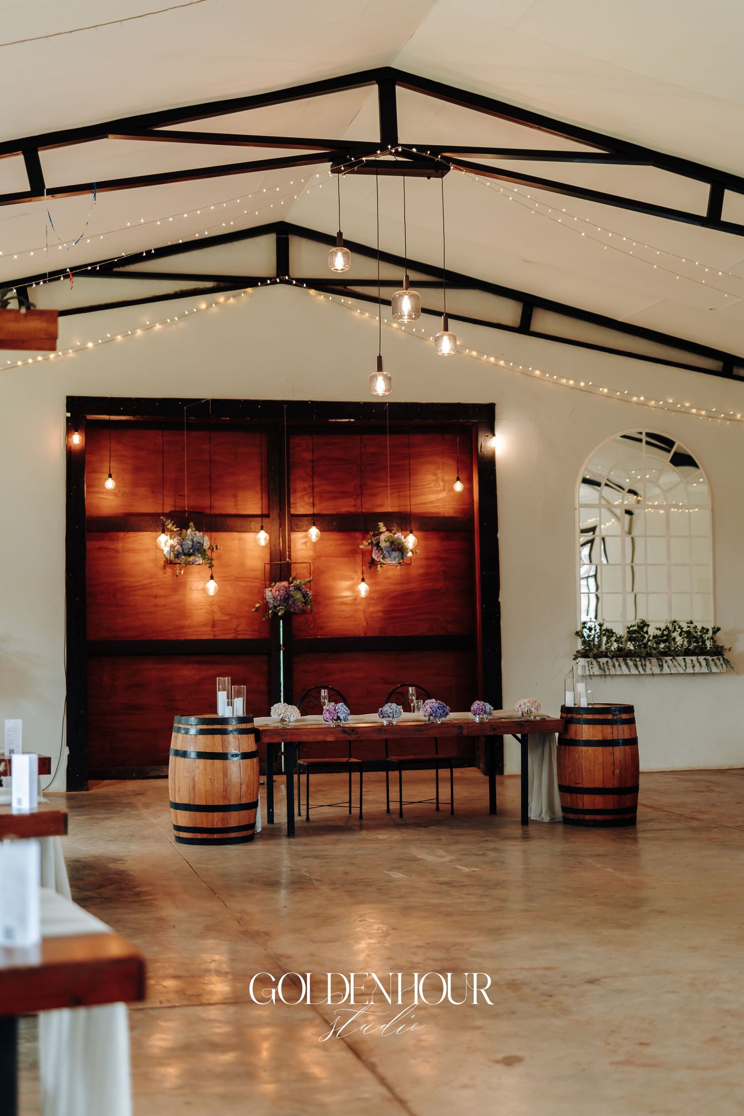 Modern rustic wedding venue interior with wooden barrels, string lights, and polished concrete floors.