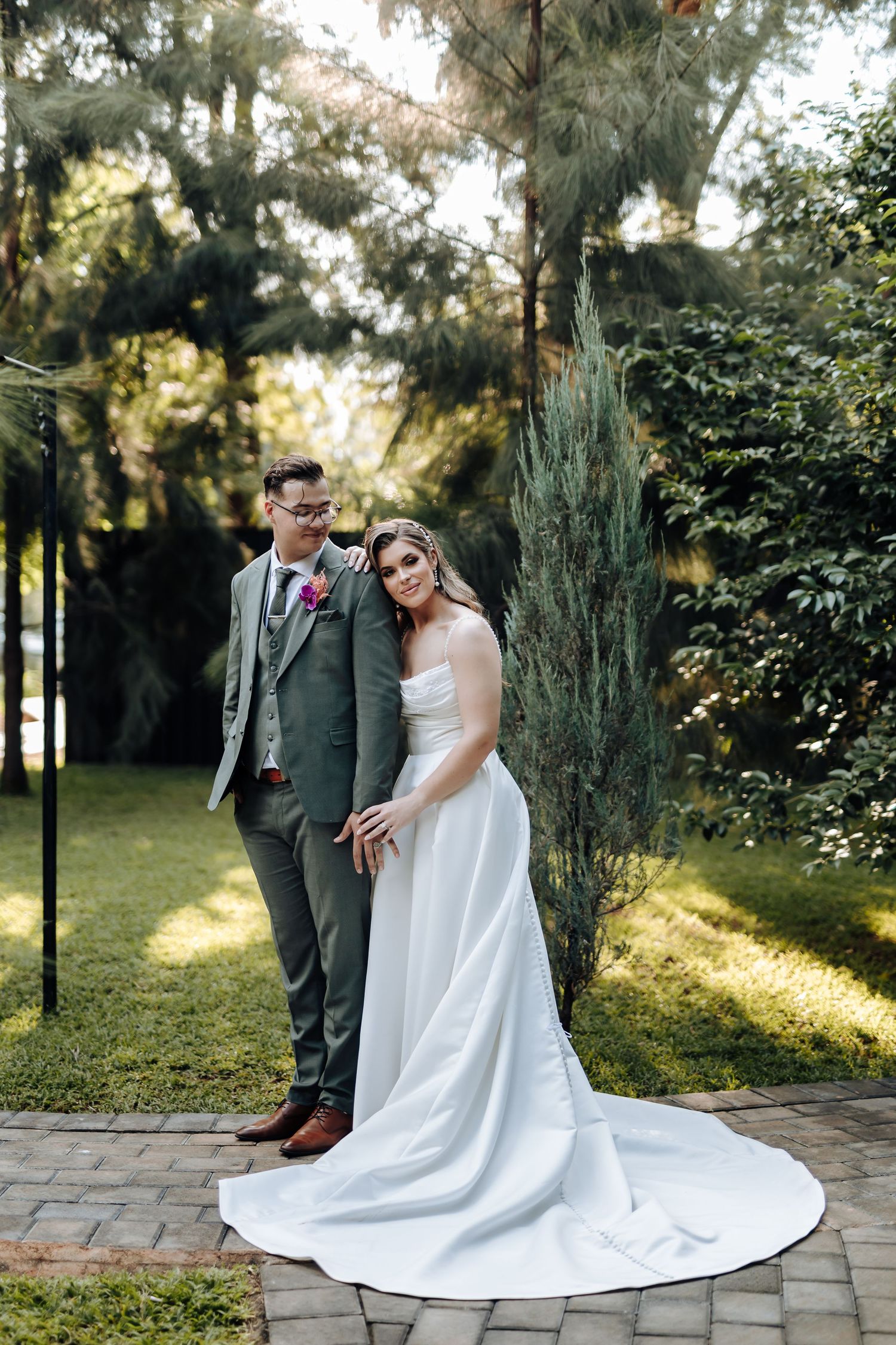 A couple shares romantic moments in a garden setting with sunlight filtering through trees during their wedding photoshoot.