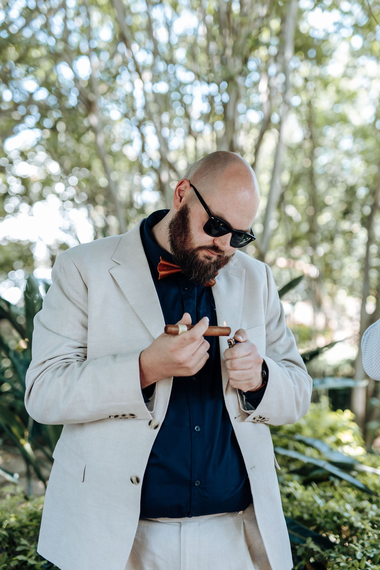 A sequence of photos showing someone in a light blazer and dark shirt lighting a cigar in an outdoor garden setting.