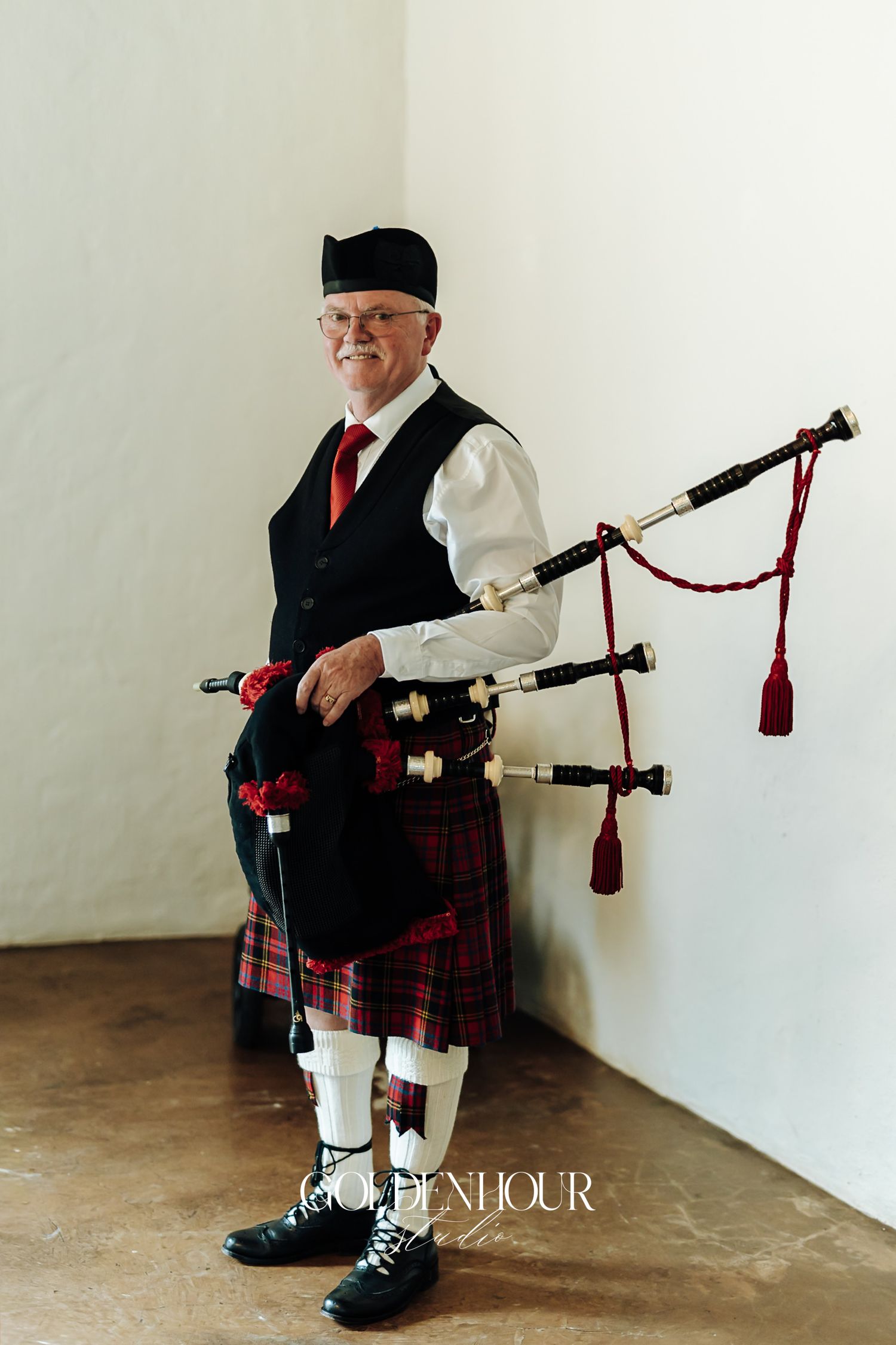 Scottish bagpiper in traditional tartan kilt and black vest holding bagpipes at a wedding.