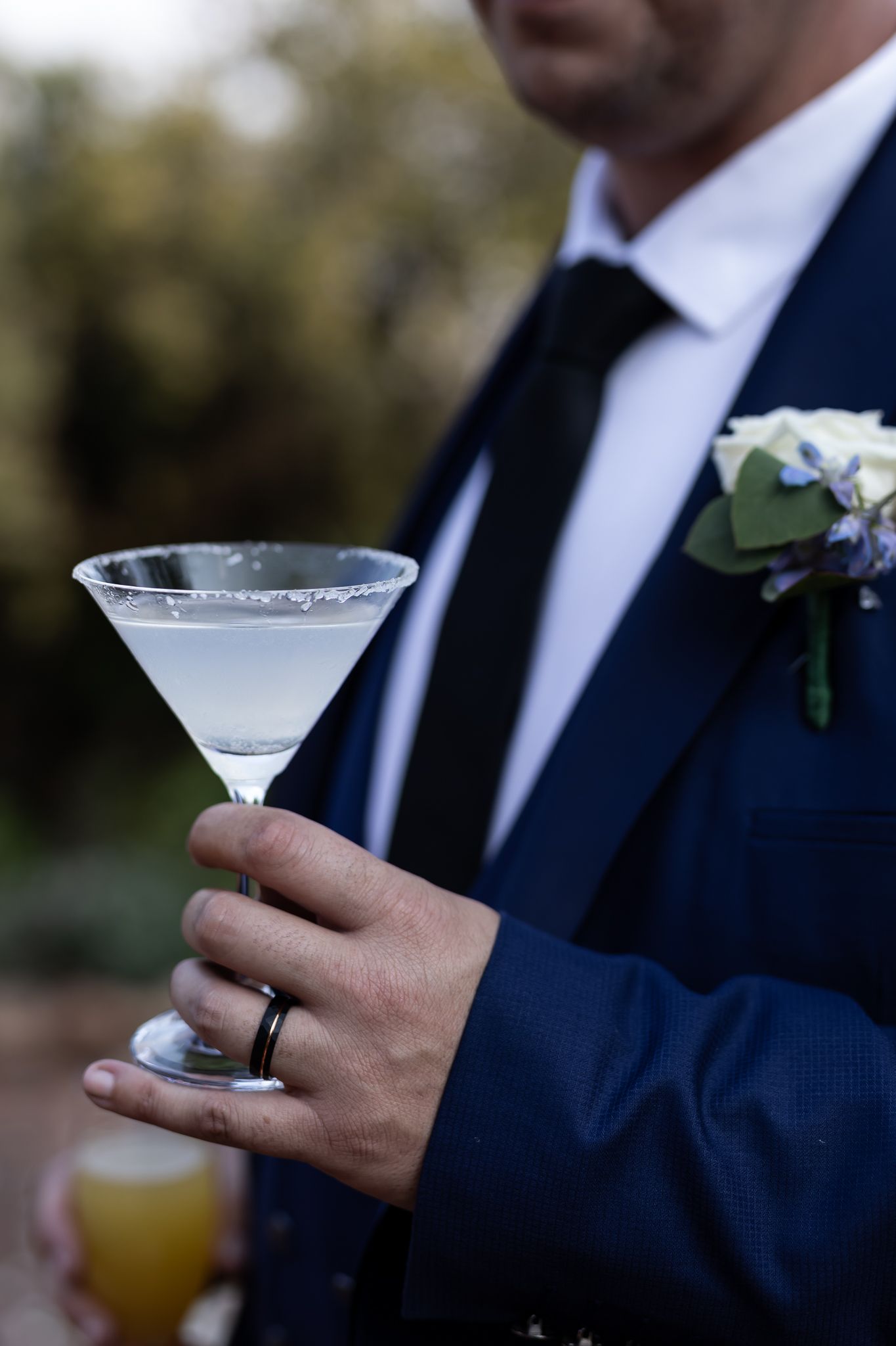 Groom in navy suit holds martini glass with sugar rim and wedding boutonniere.
