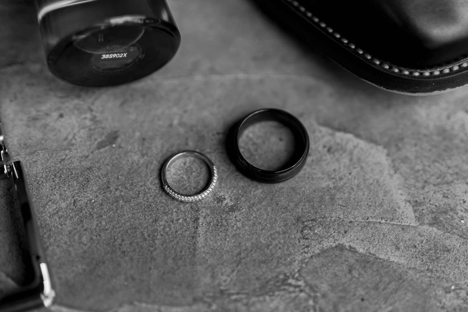 Two wedding rings photographed in black and white on a textured surface.