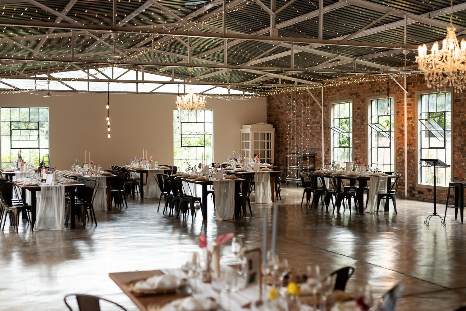 Industrial chic wedding reception venue with exposed brick, chandeliers and elegant table settings.