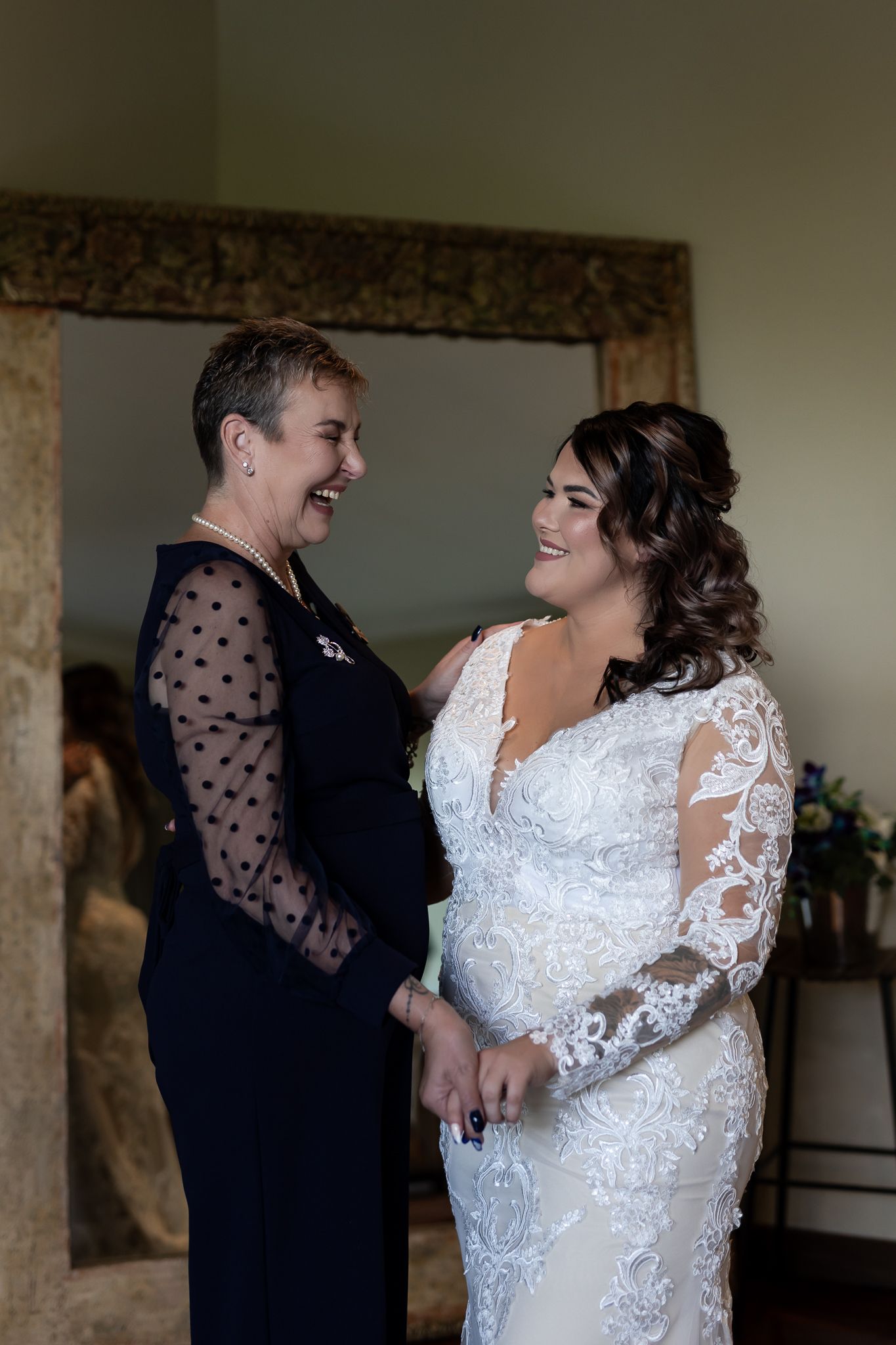 Joyful moment shared during wedding preparations in front of ornate mirror.
