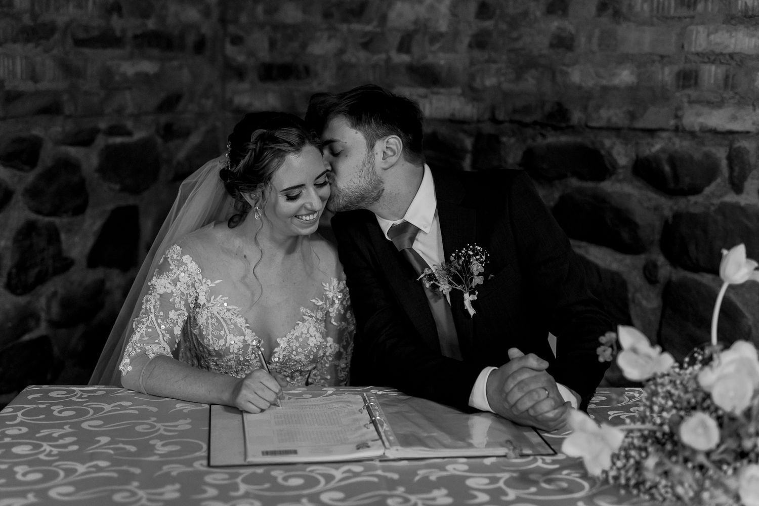 Intimate black and white moment captured during wedding ceremony signing at decorated table.
