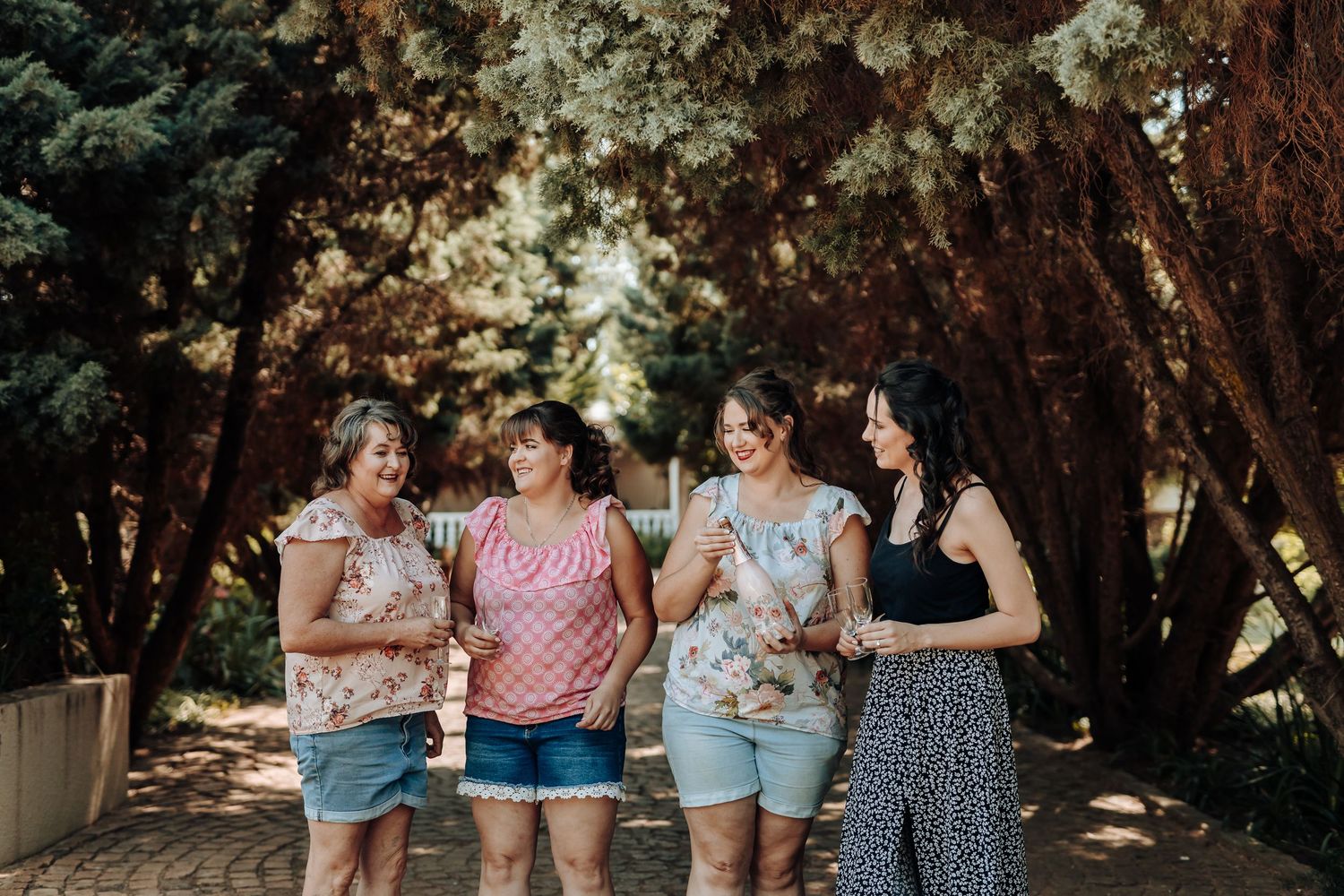 Four friends enjoying drinks together under tree-covered pathway.
