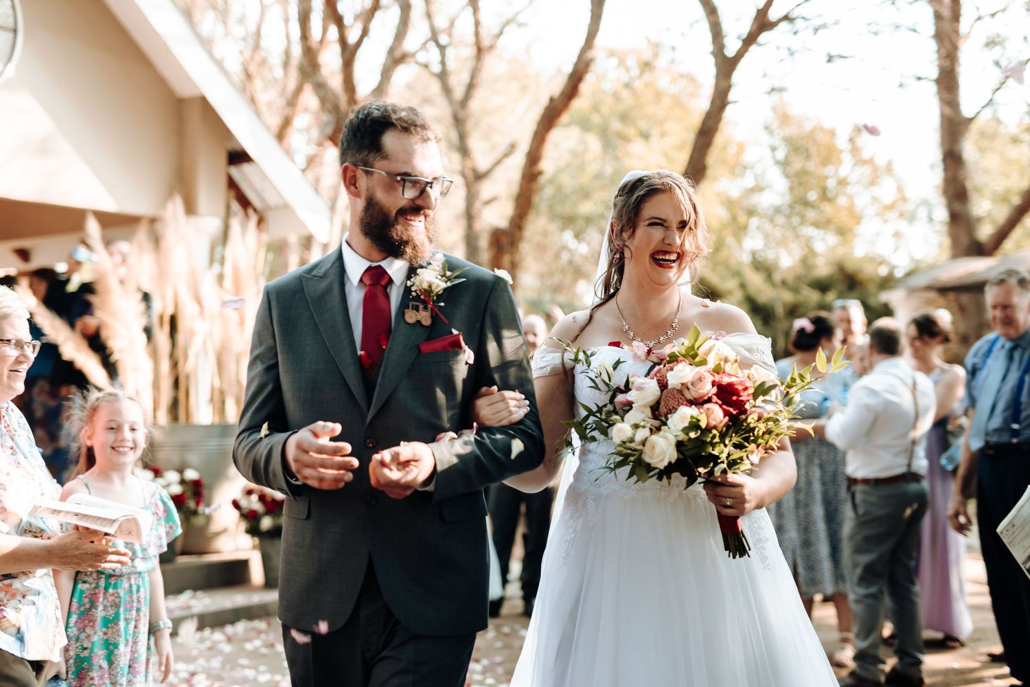 A wedding couple shares a candid moment during their outdoor reception while holding glasses and a bouquet.
