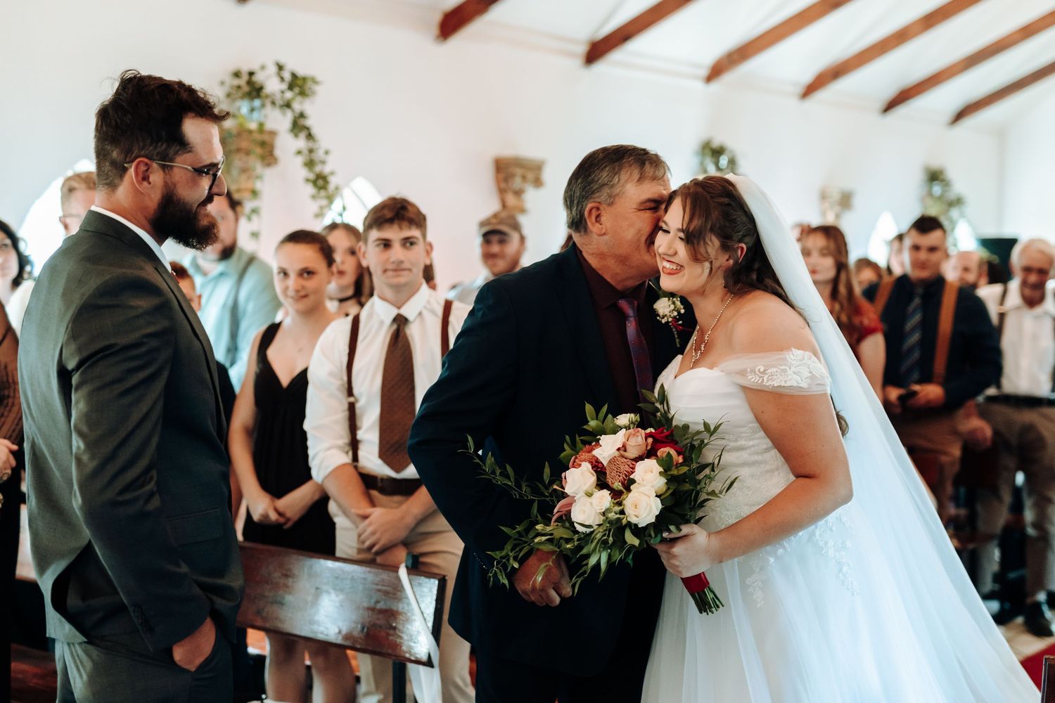 Emotional moment during wedding ceremony inside white chapel with wooden ceiling beams.