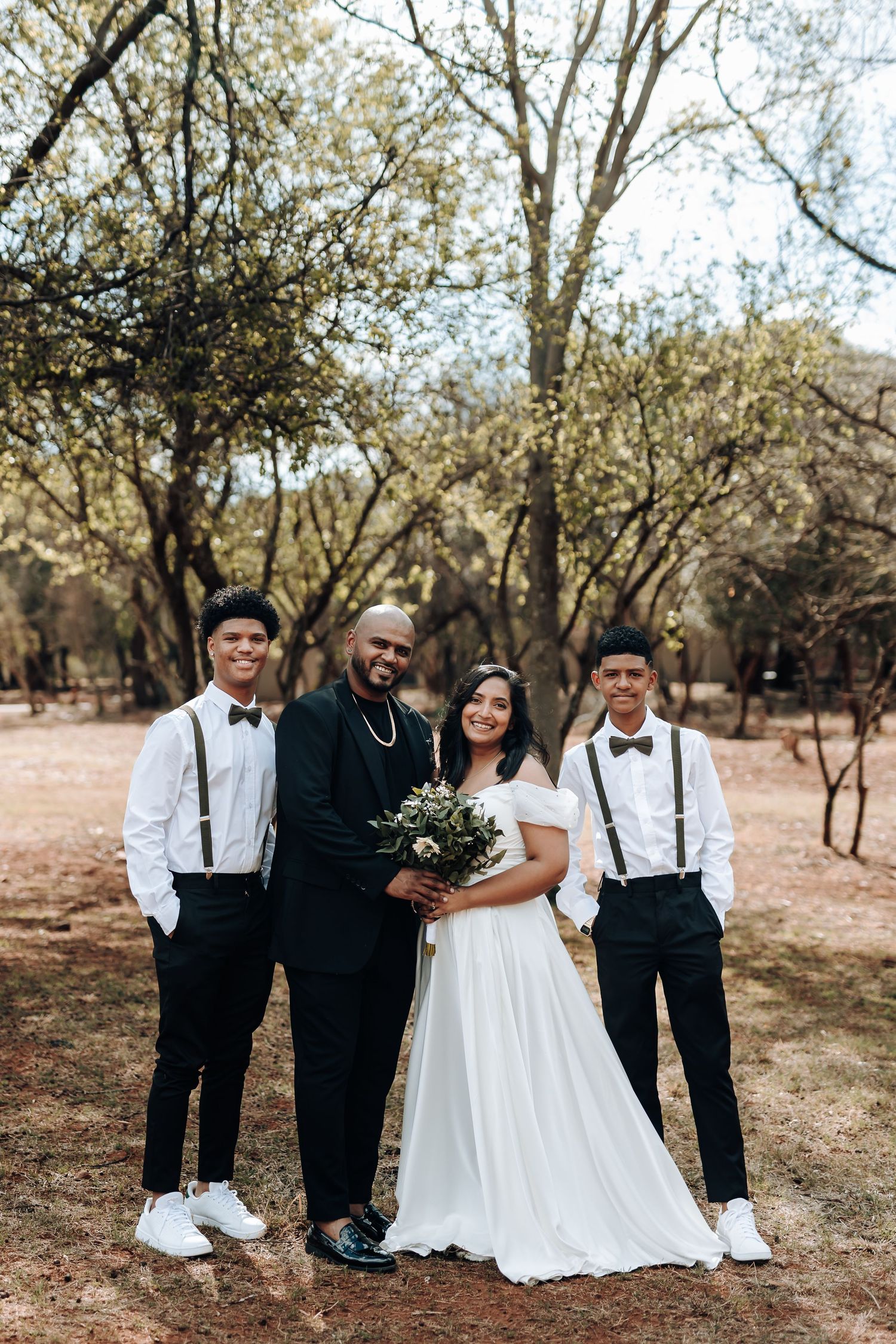 Wedding party in black and white attire poses together in outdoor woodland setting.