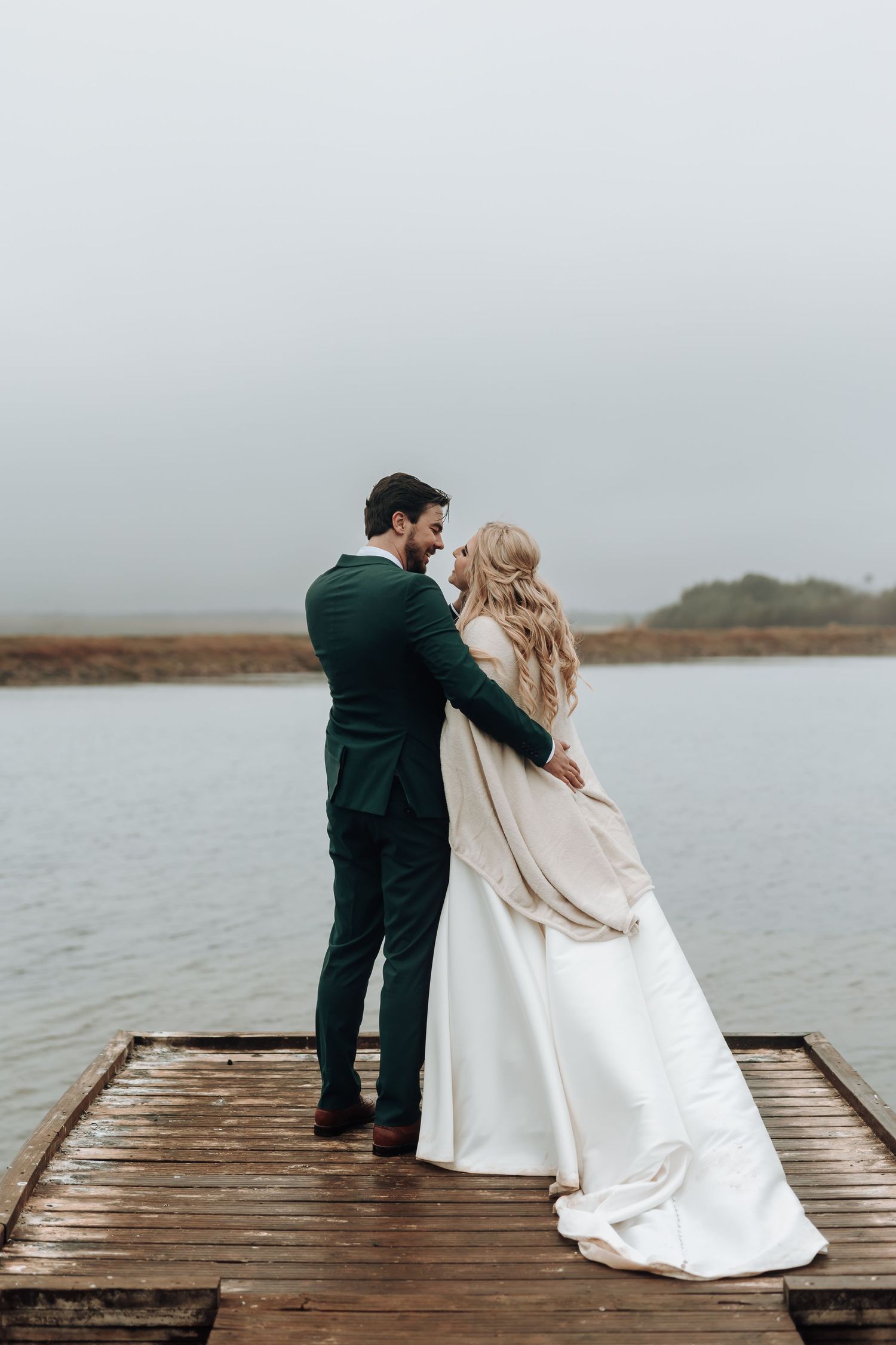 Romantic moment between newlyweds on wooden pier with water views.