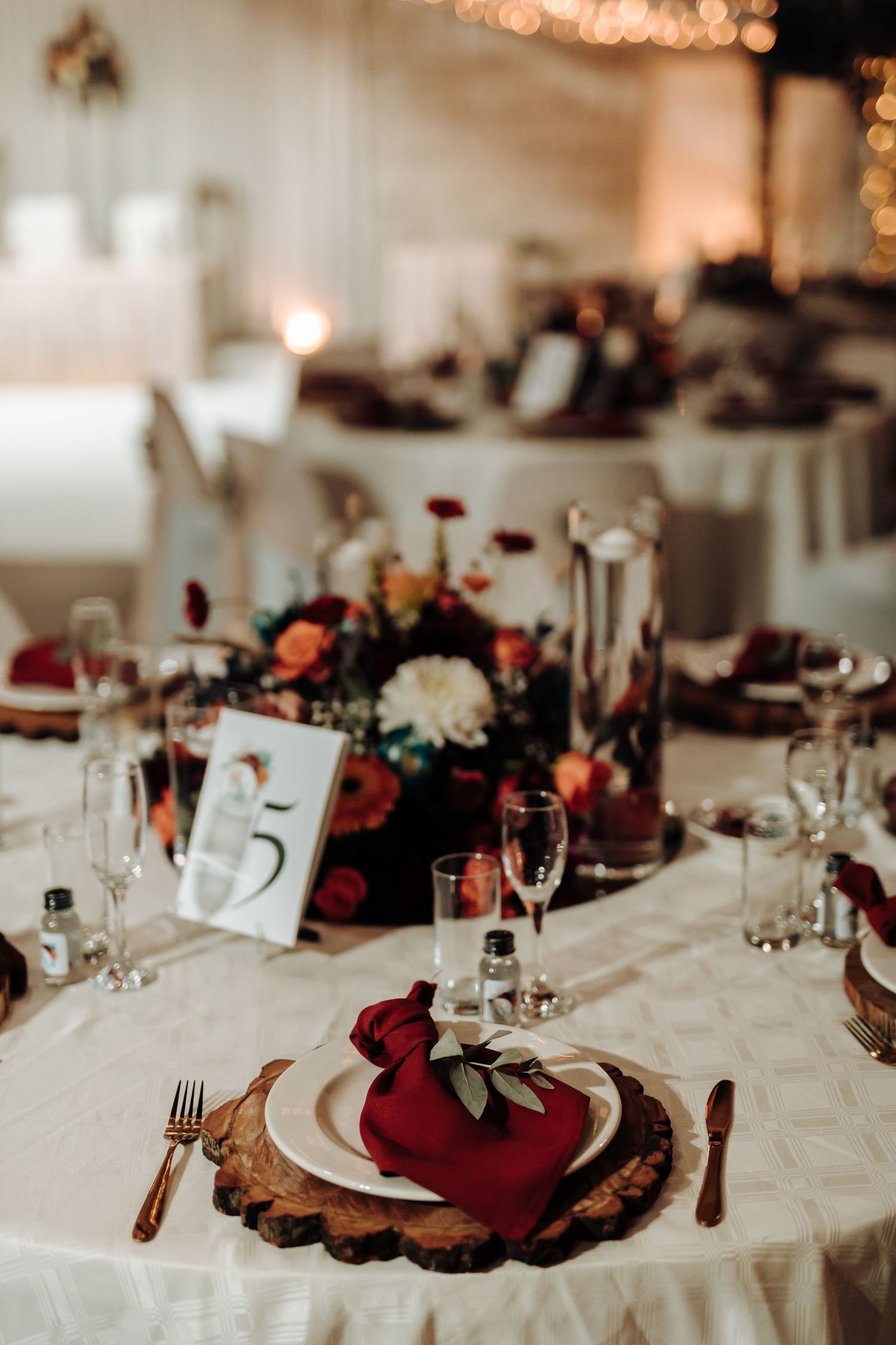 Wedding table setting with burgundy napkin, wooden charger plate, and romantic floral centerpiece.