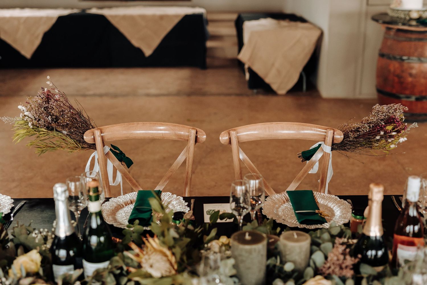 Wedding reception detail of wooden chairs with green napkins and floral decorations.