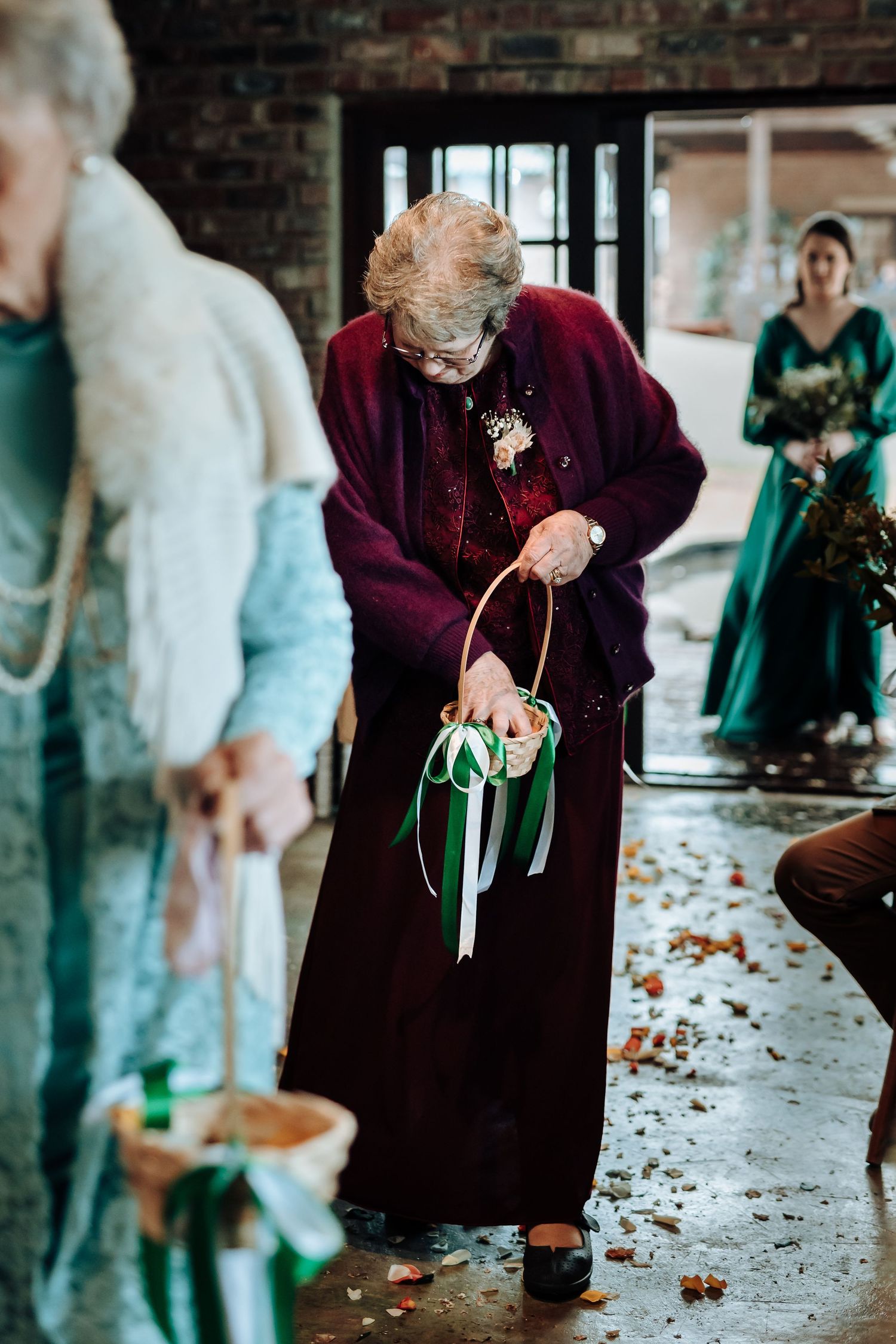 An elderly attendee in a deep burgundy dress carrying a floral bouquet with green ribbons.
