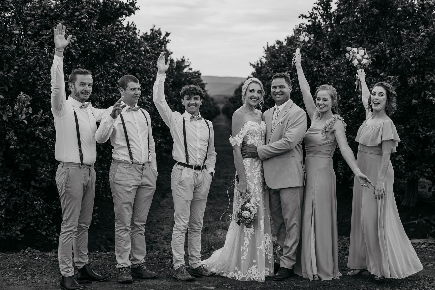 Black and white photo of wedding party celebrating with arms raised outdoors.