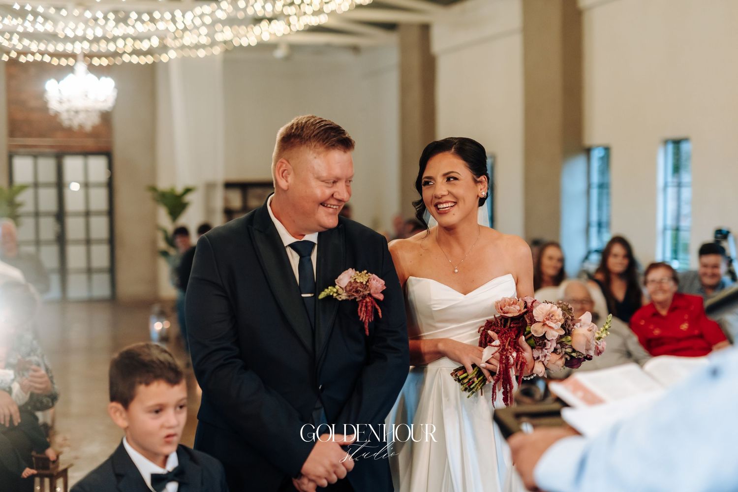 Smiling bride and groom standing together during wedding ceremony with young boy nearby.