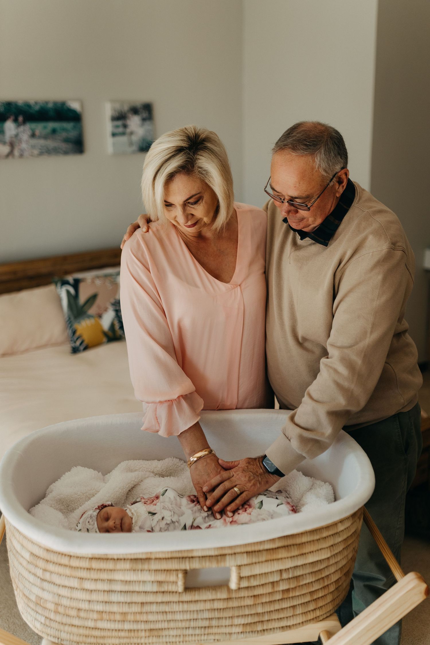 A couple in soft pastel clothing sits together by a woven basket Moses bed, sharing an intimate moment.