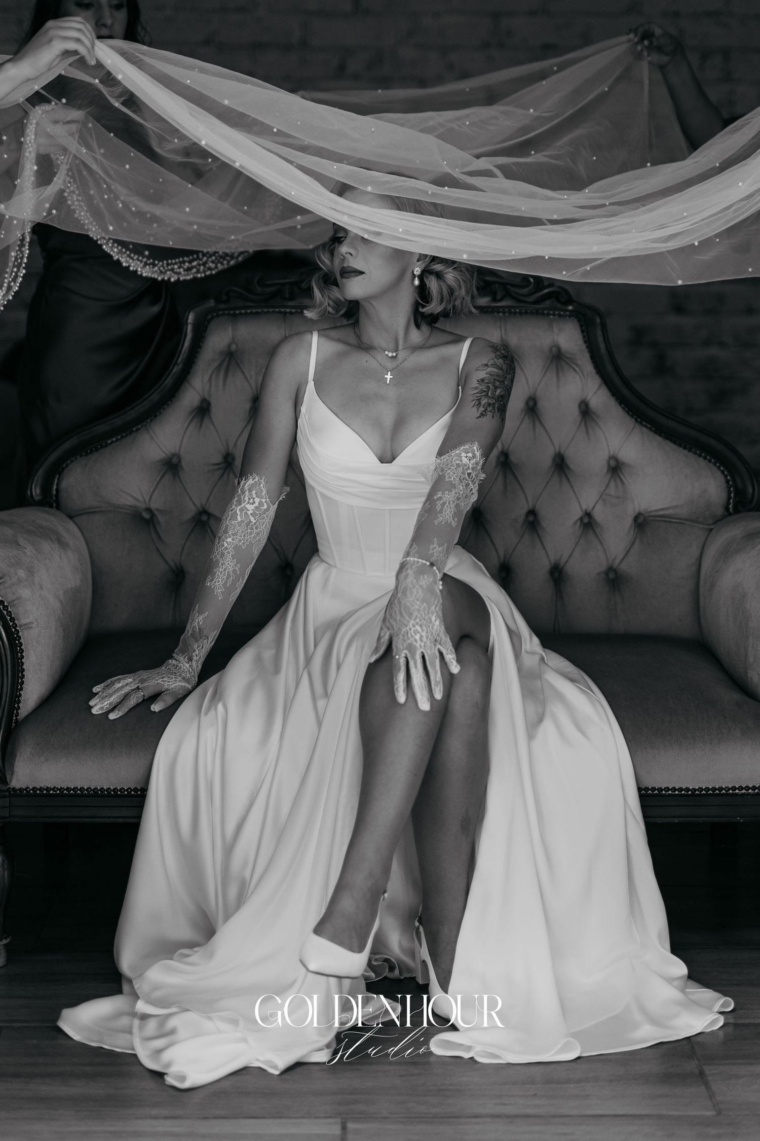 Black and white photo of wedding dresses and formal attire arranged on an elegant tufted sofa.