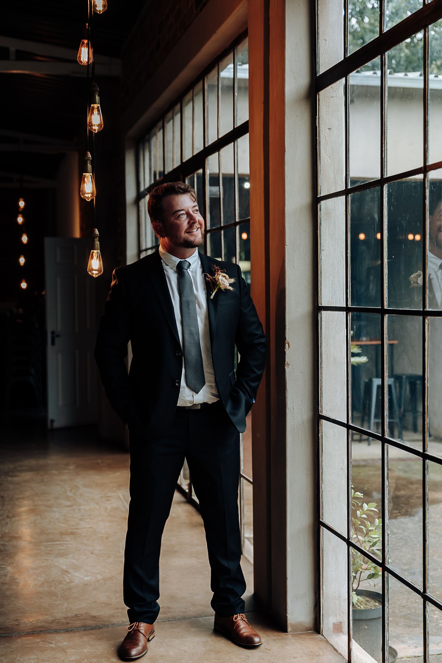 Stylish brown leather dress shoes paired with dark suit pants stand near floor-to-ceiling windows in modern venue.