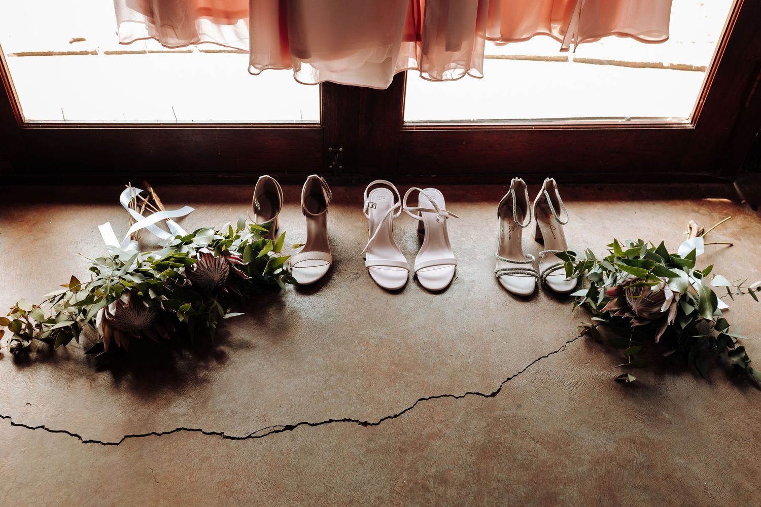 Pairs of dress shoes and sneakers arranged in a row along a hardwood floor with holiday greenery decorations.