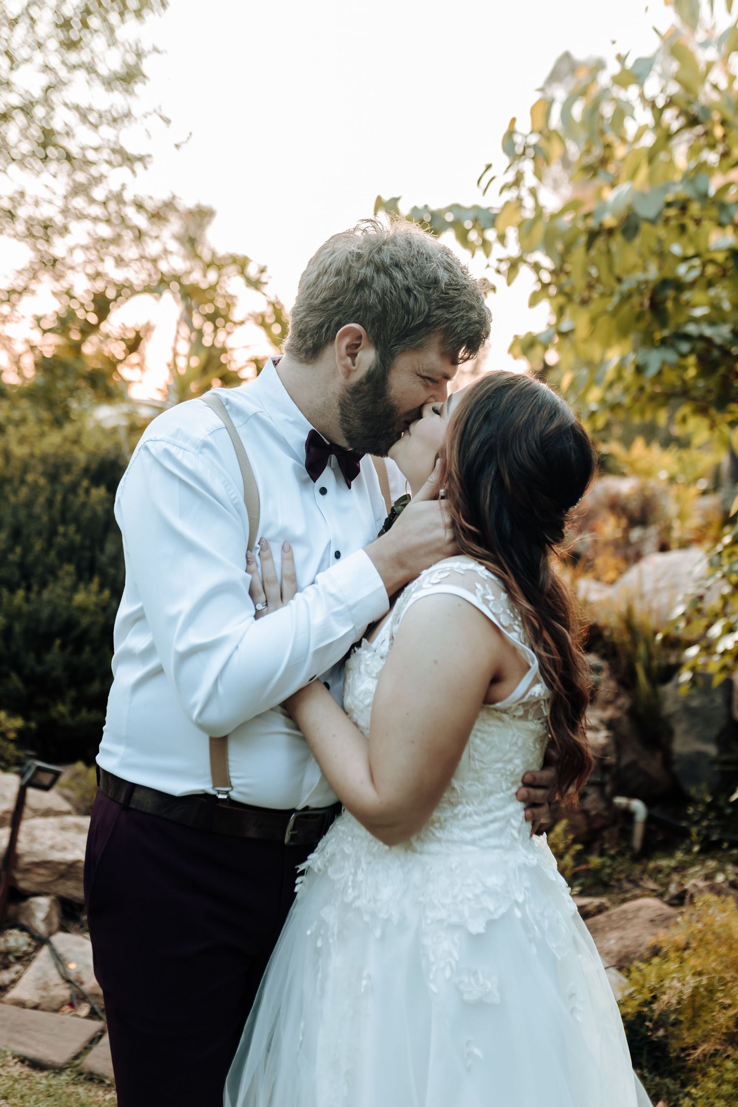 Romantic sunset wedding photo of couple sharing tender moment in garden setting.