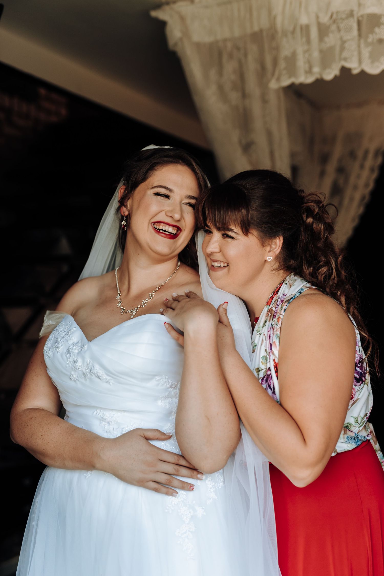 A joyful wedding moment capturing shared laughter between a bride and guest in a red dress.