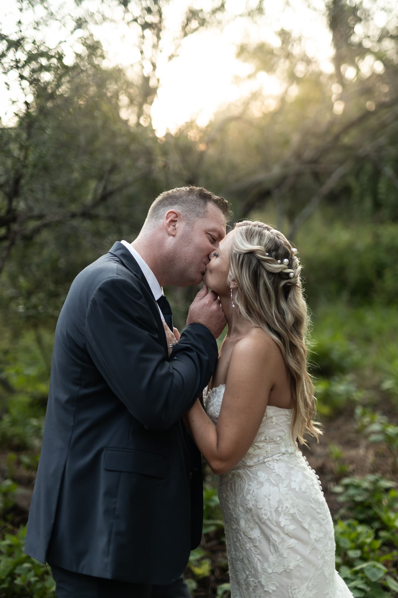 A tender kiss shared between newlyweds in a sunlit garden setting.