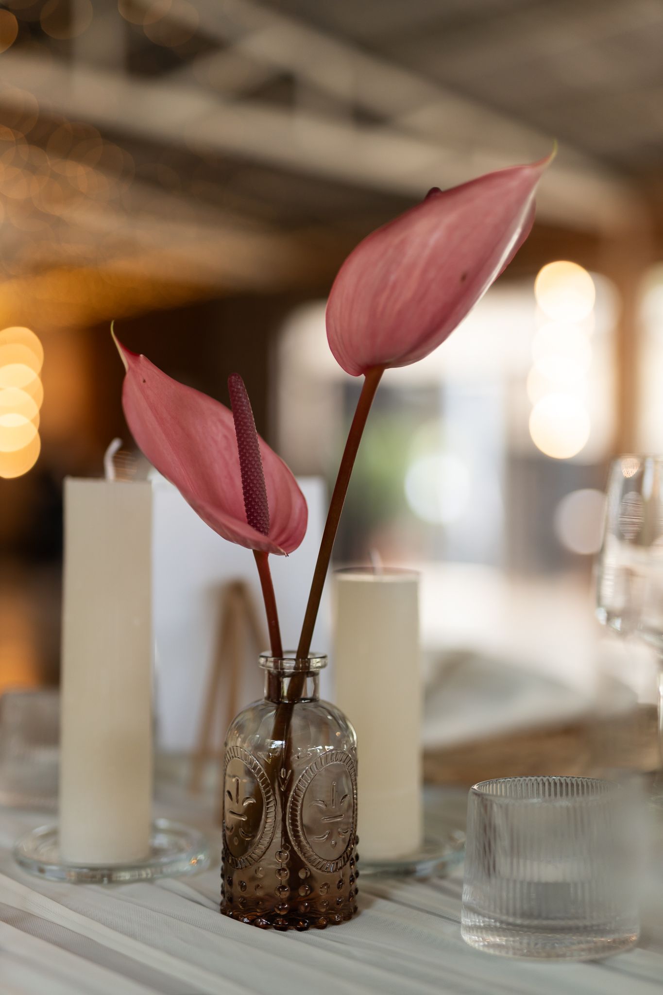 Two pink anthurium flowers in a vintage brown glass vase with soft bokeh lighting.