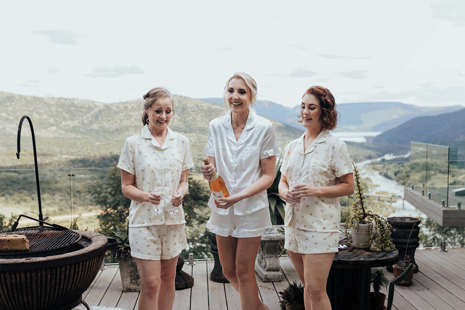 Friends in matching white loungewear enjoying drinks on scenic mountain terrace.