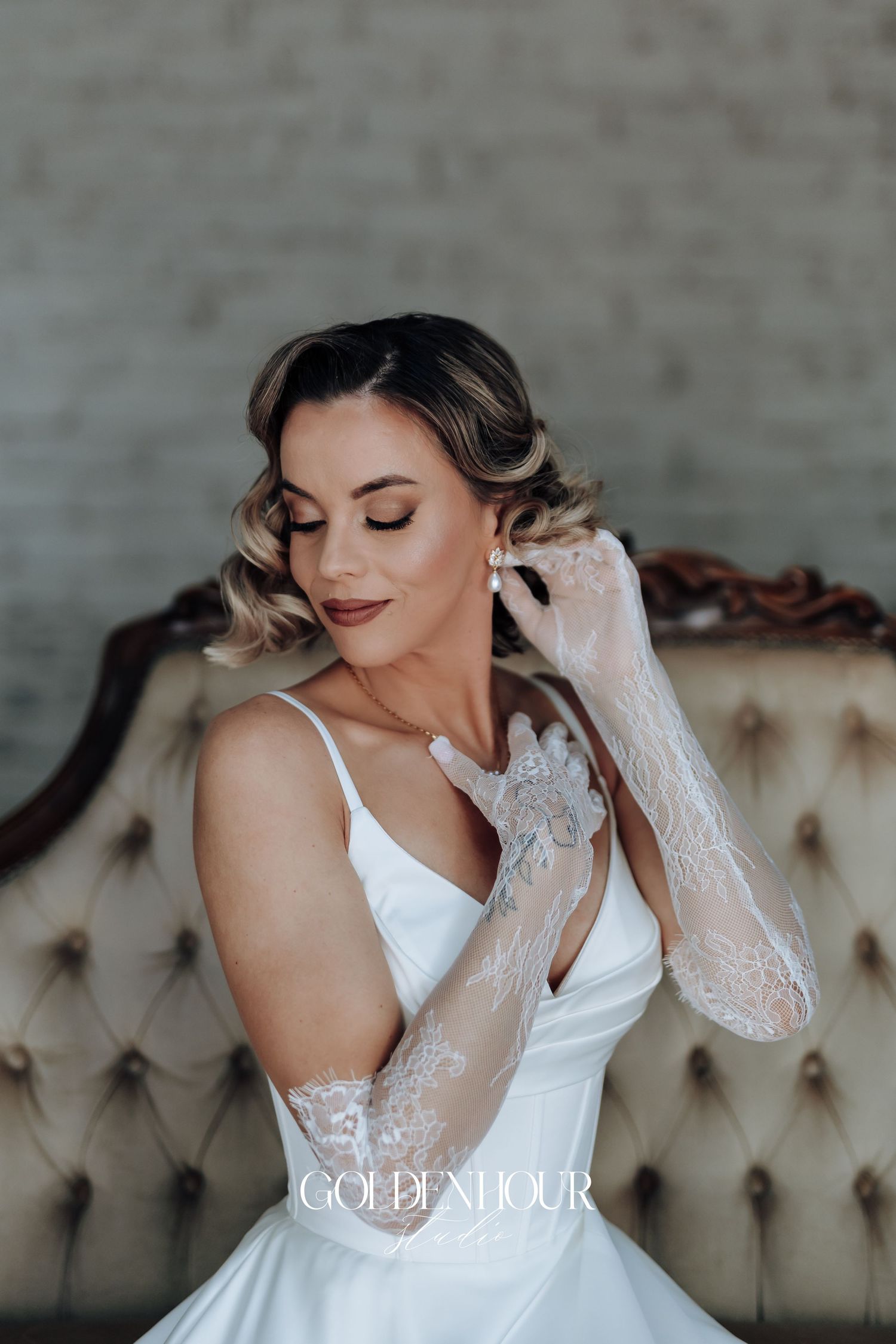 Bride in elegant white lace gown poses against neutral backdrop.