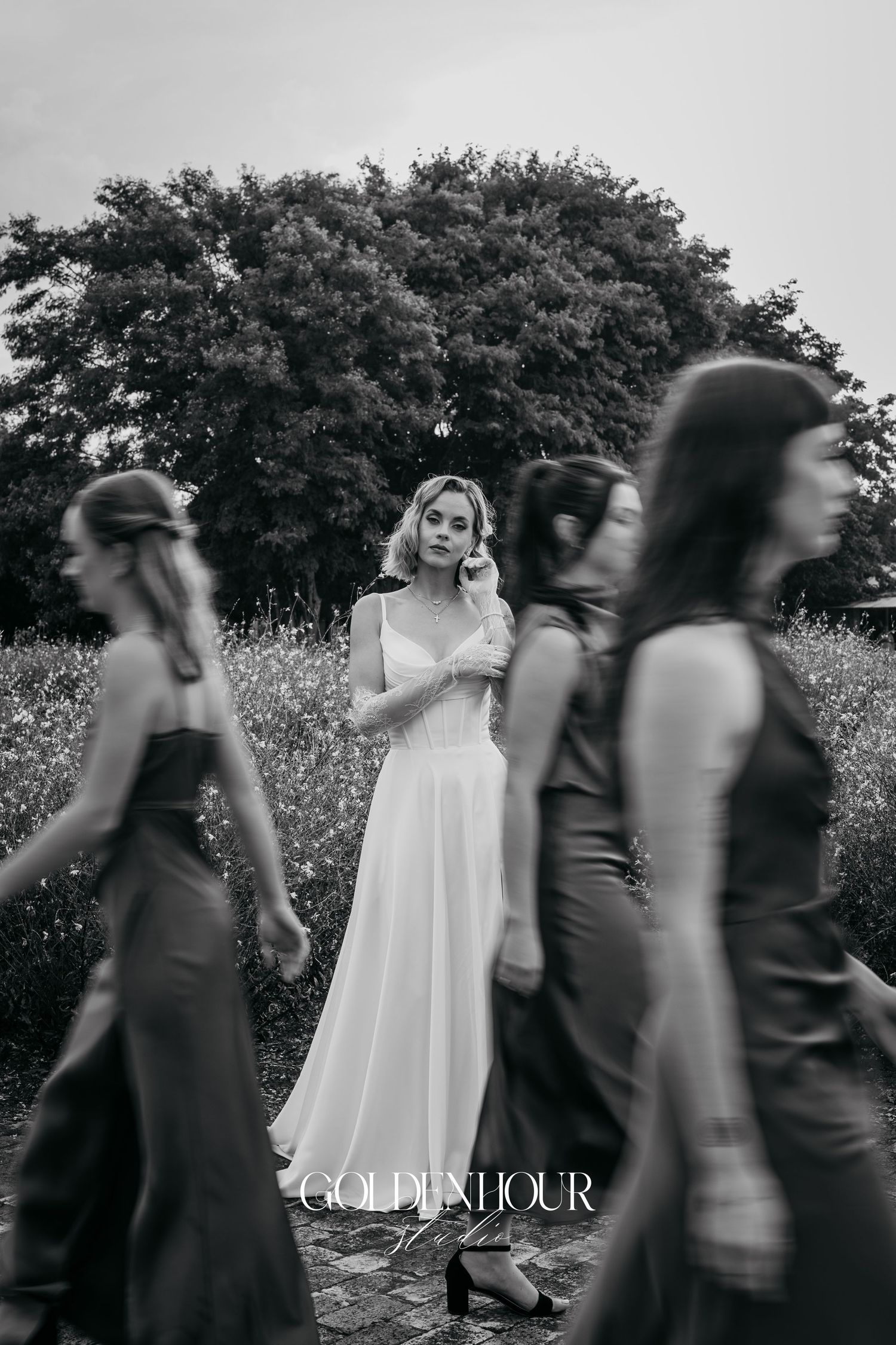 Artistic black and white photo of bridesmaids walking past bride in flowing dress.