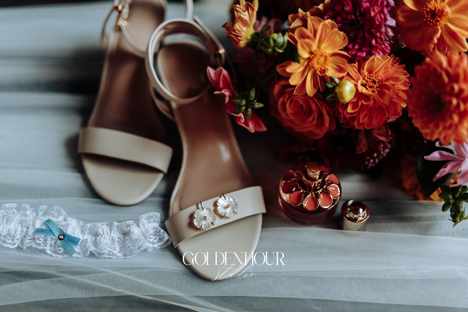 Wedding flat lay featuring nude sandals, jeweled garter, orange floral bouquet, and gold accessories.