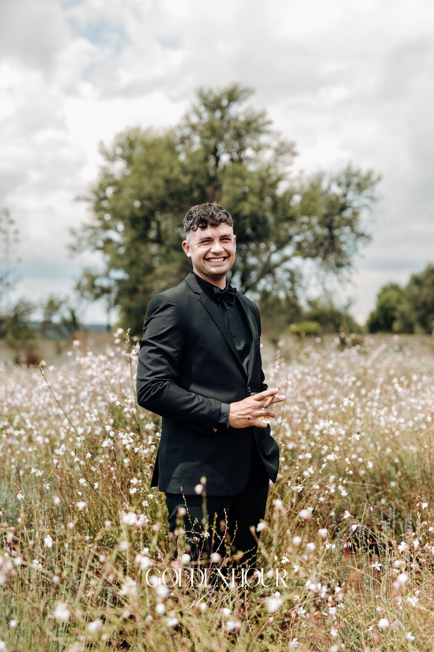 A person in black clothing sits joyfully in a field of white wildflowers on an overcast day.